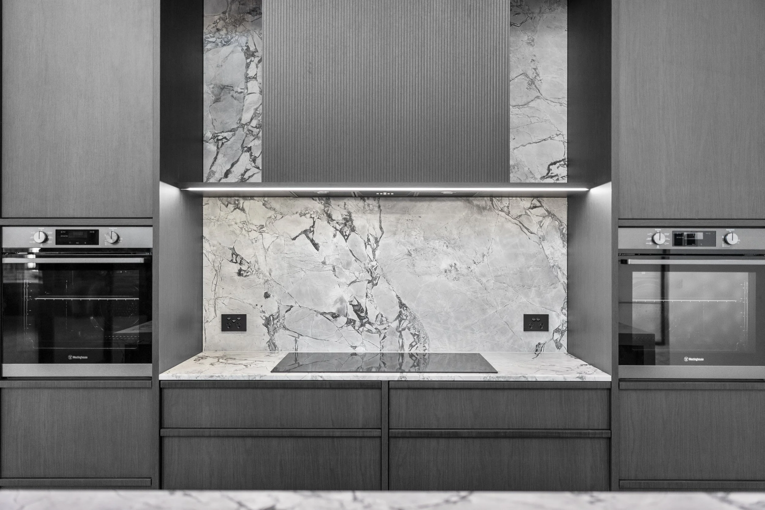 Modern kitchen backsplash with a mix of dark and light marble and textured metal panels.