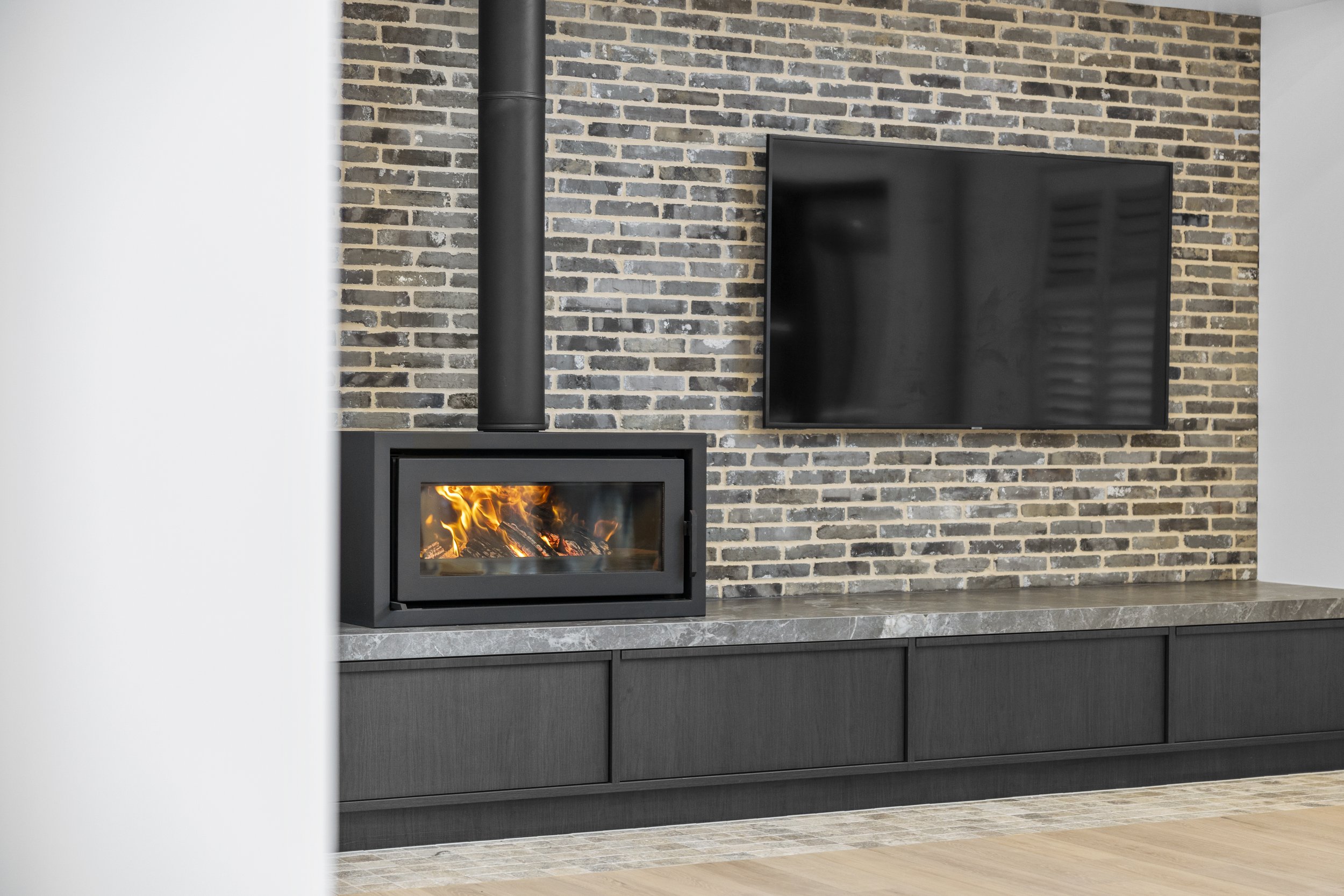 Modern living room with a black fireplace, a mounted TV on a brick wall, and sleek dark cabinetry beneath the fireplace.