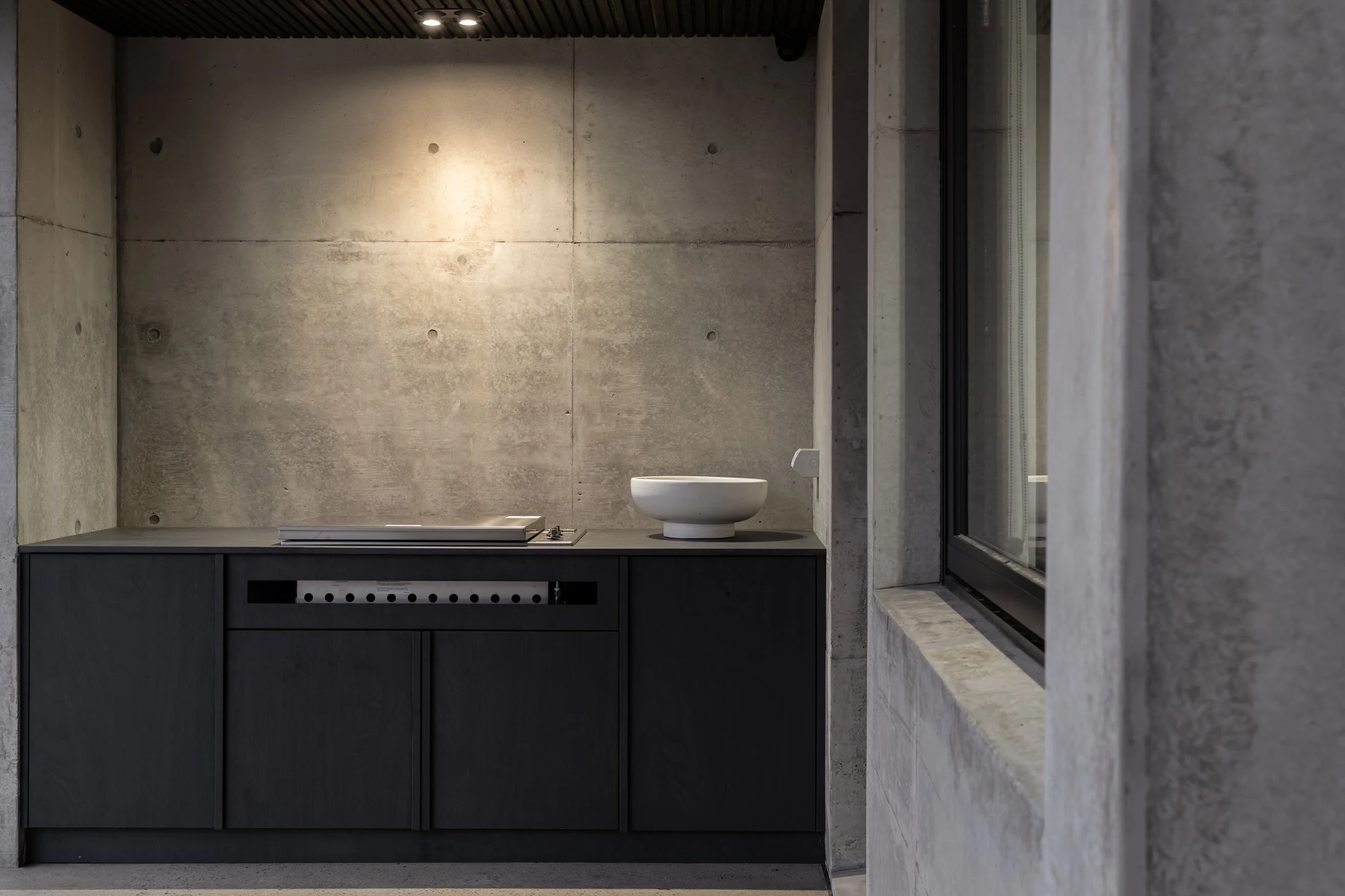 Modern bathroom with concrete walls, a white vessel sink, dark vanity, and a large window with a black frame.