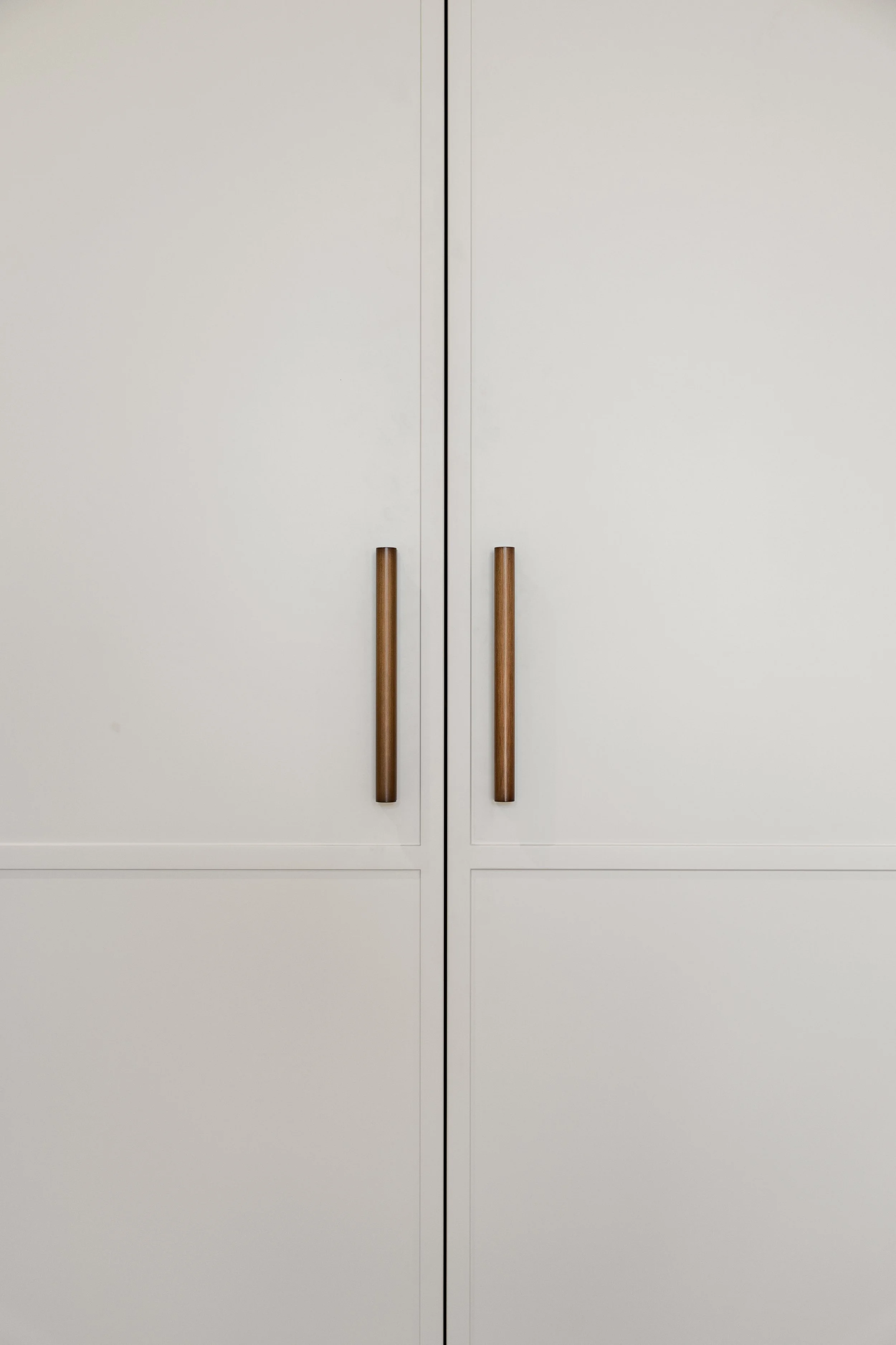 White closet/ storage doors with vertical wooden handles.