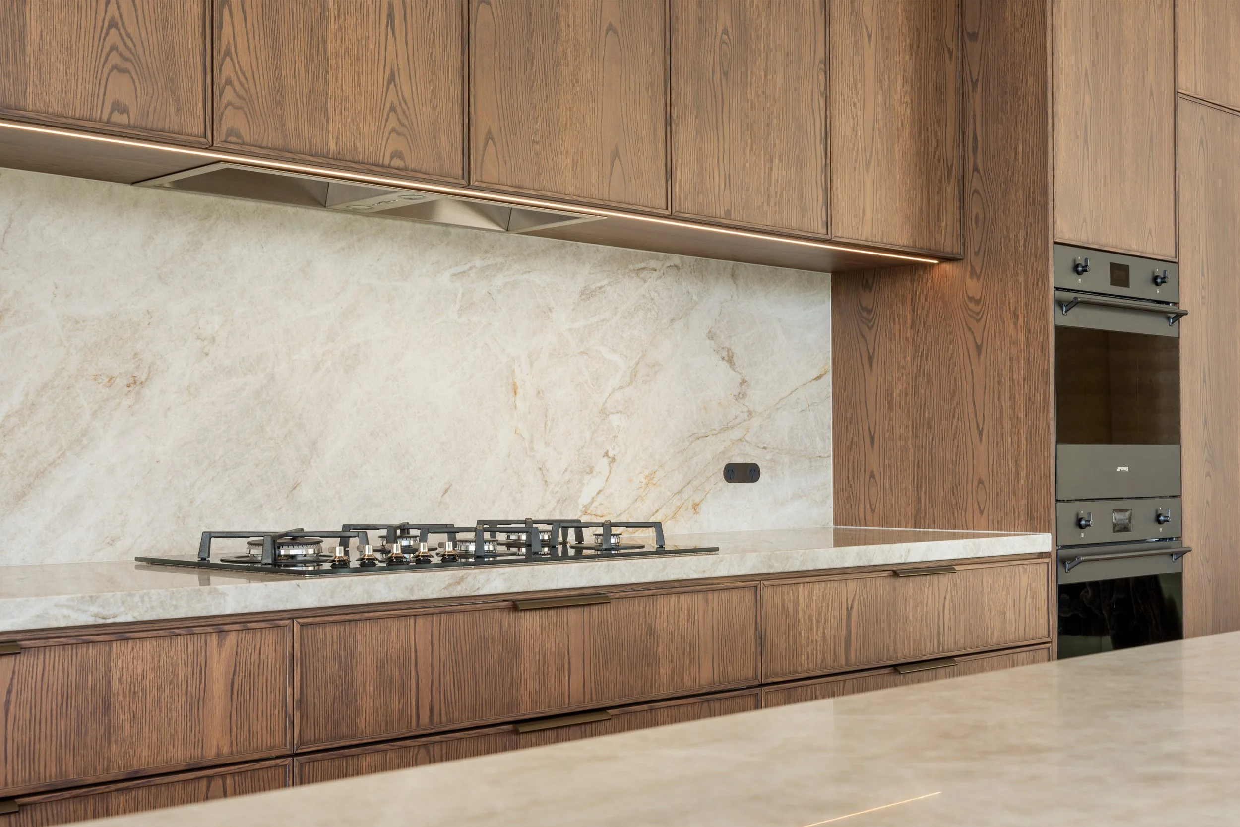 Kitchen with wooden cabinets, beige marble backsplash, gas stove, and stainless steel oven.