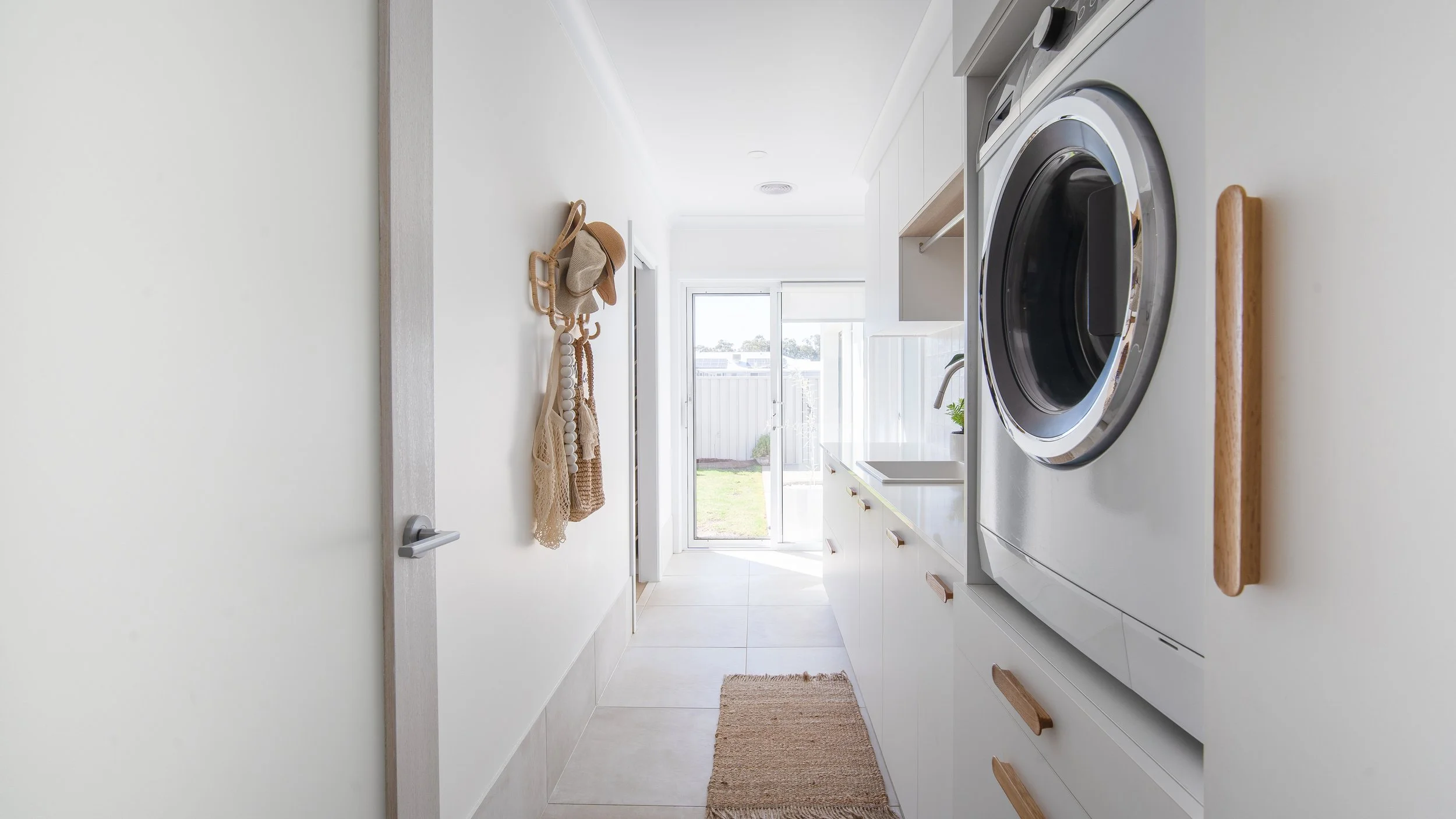 Laundry room with white cabinets, a washing machine, a wooden cutting board on top, a beige rug, and a view of the backyard through a sliding glass door.