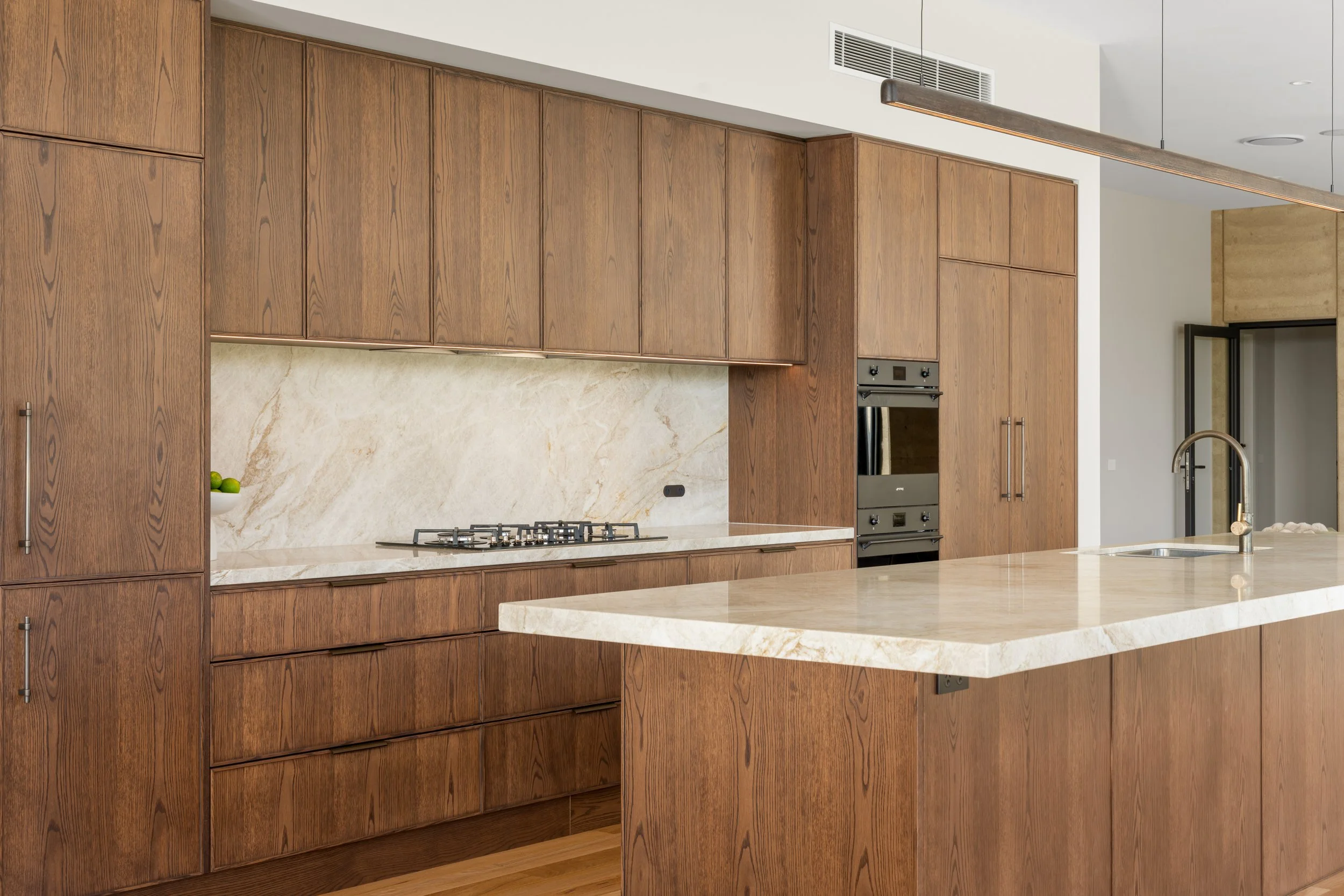 Modern kitchen with wooden cabinetry, marble backsplash, a gas cooktop, and an island counter with a sink.