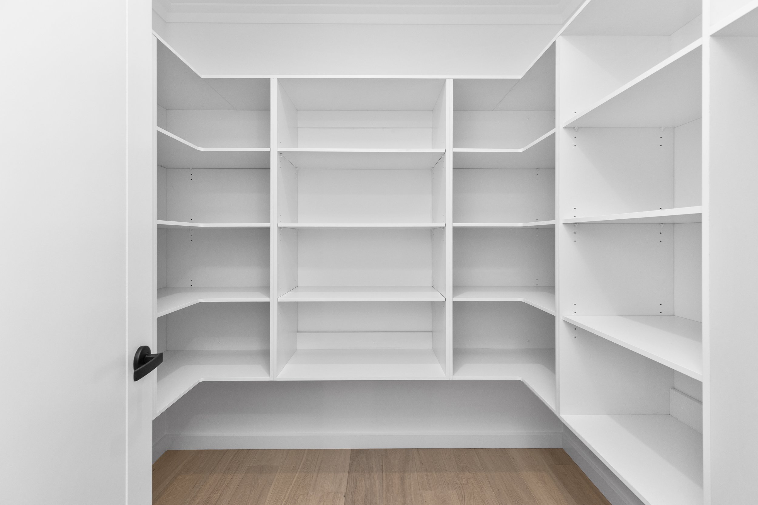 Empty white built-in bookshelf with multiple shelves in a room with wooden floor and doors open