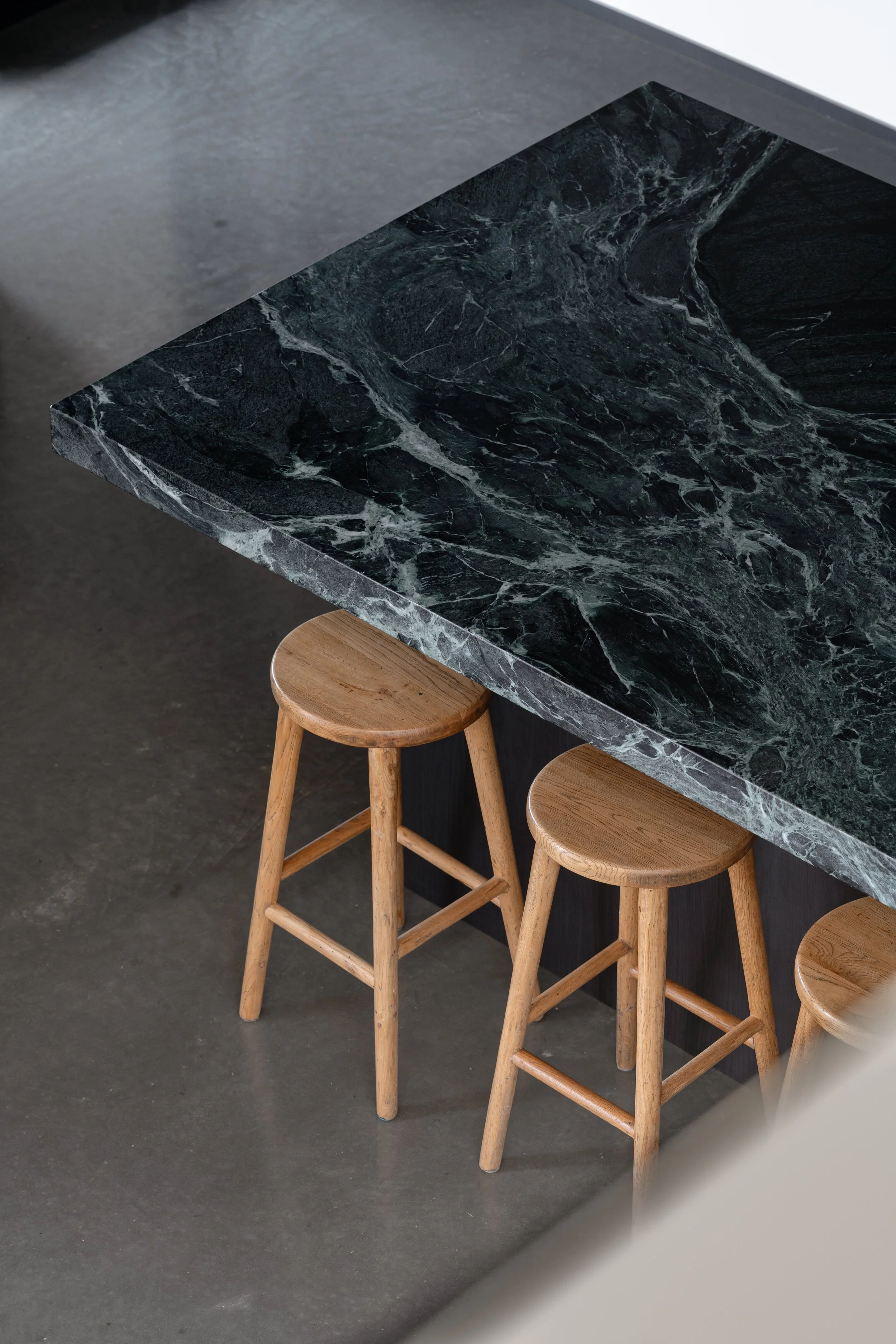 Close-up of a black marble countertop with white veining, supported by wooden barstools, in a modern kitchen or cafe setting.
