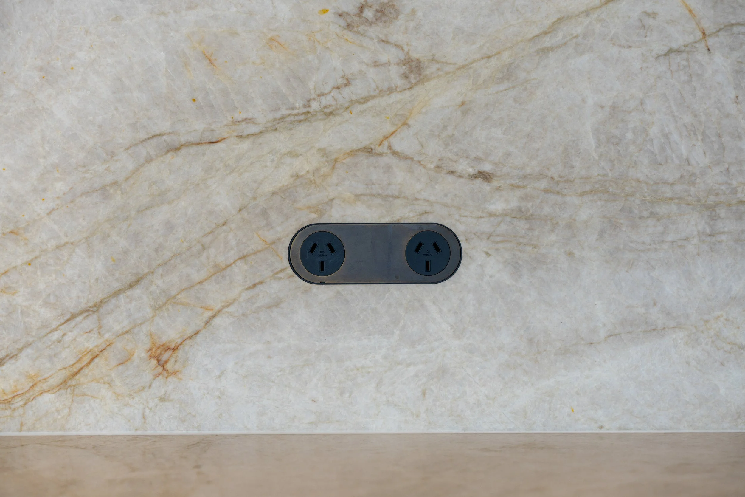 Close-up of a beige marble countertop with two electrical outlets.
