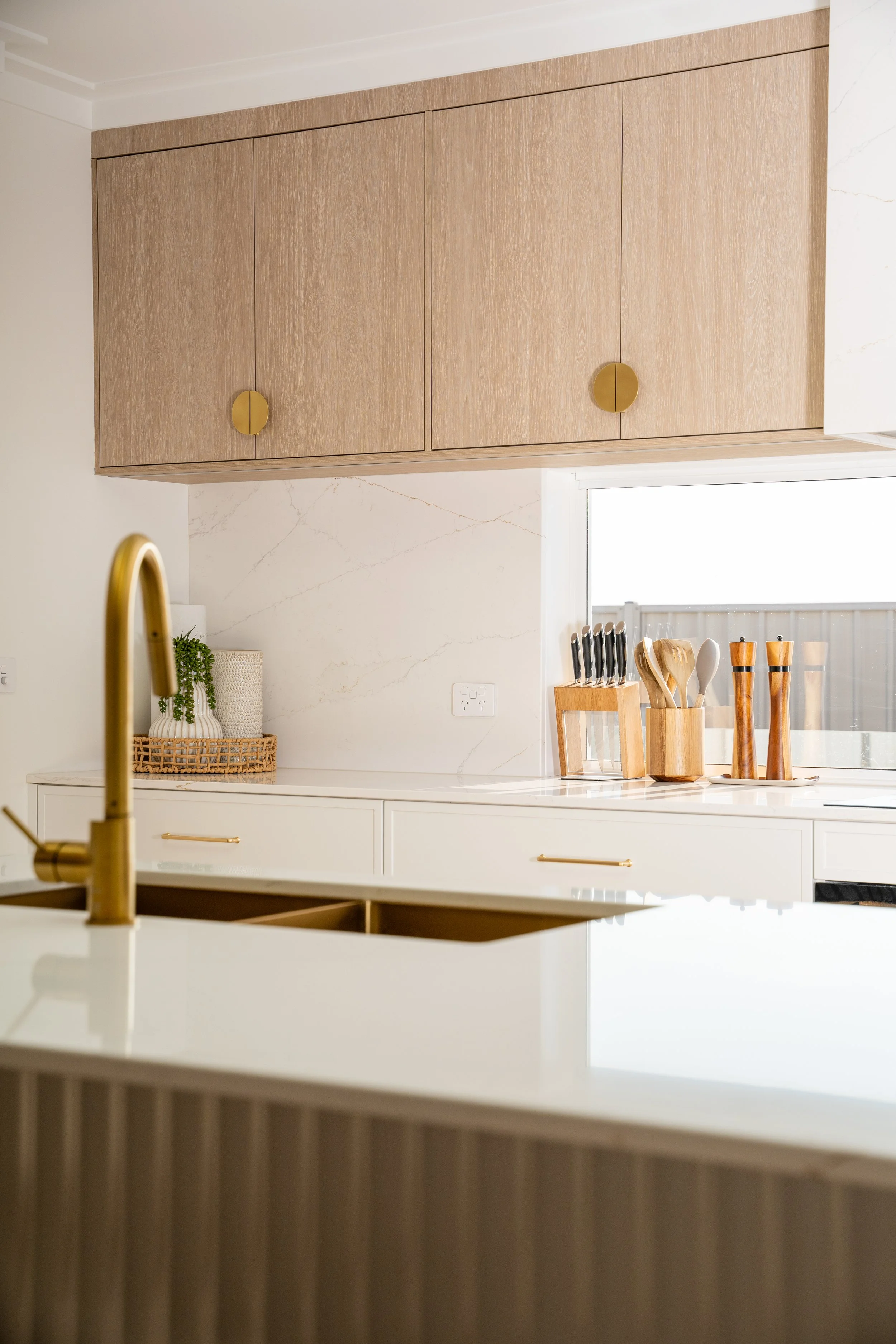 Kitchen with light wood upper cabinets, a white marble backsplash, and a countertop with kitchen utensils in a wooden container.
