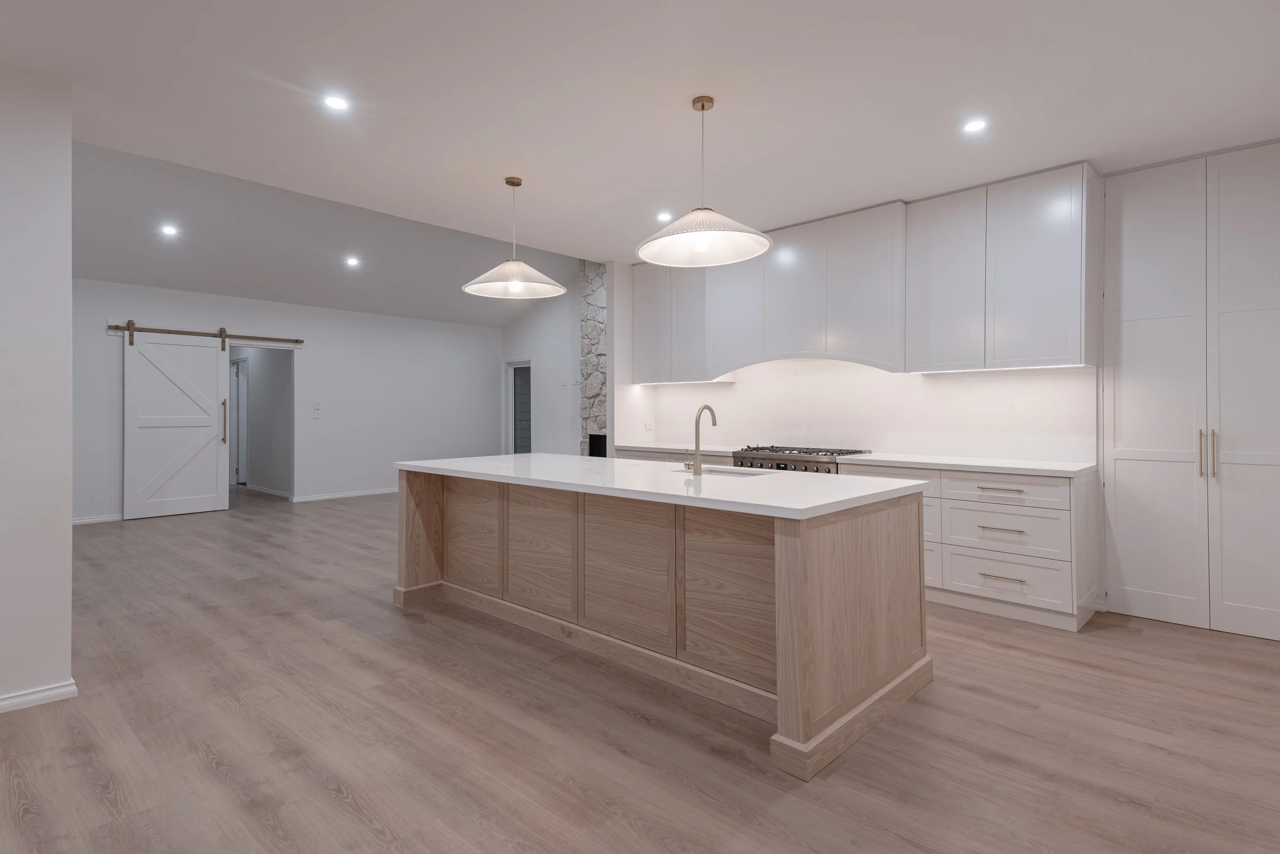 Modern kitchen with white cabinets, a large central island with a white countertop and wood paneling, light wood flooring, and pendant lights hanging from the ceiling.