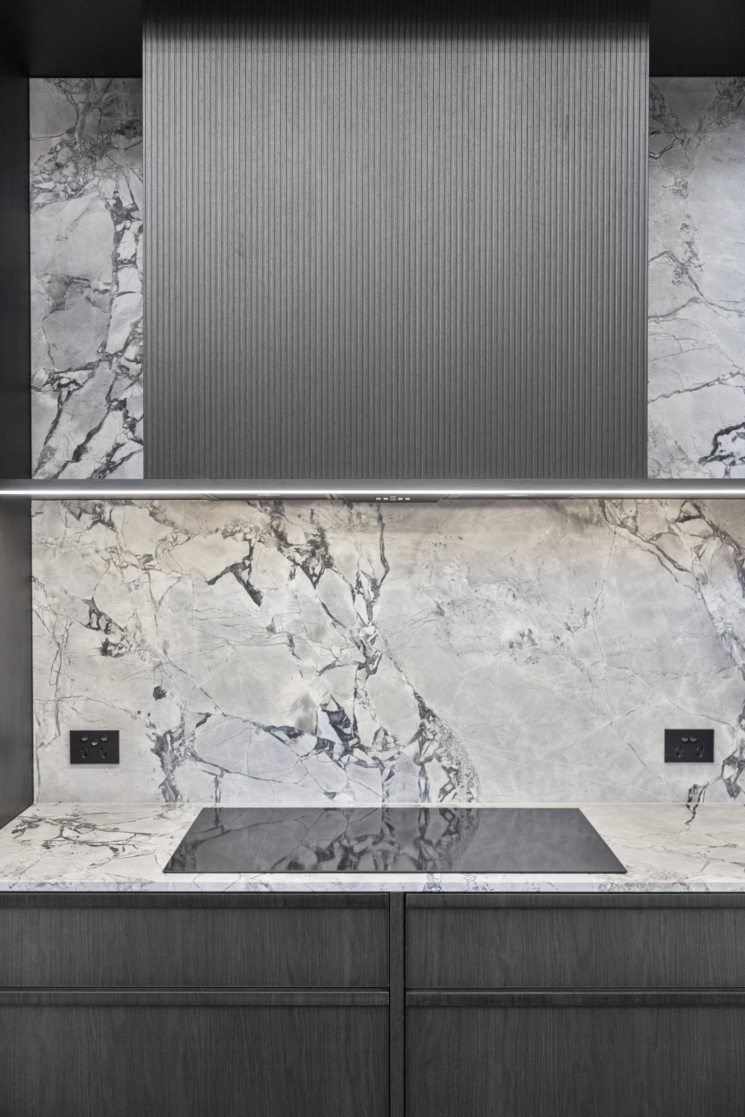 Modern kitchen backsplash with a large marble slab, dark cabinetry, and an induction cooktop.