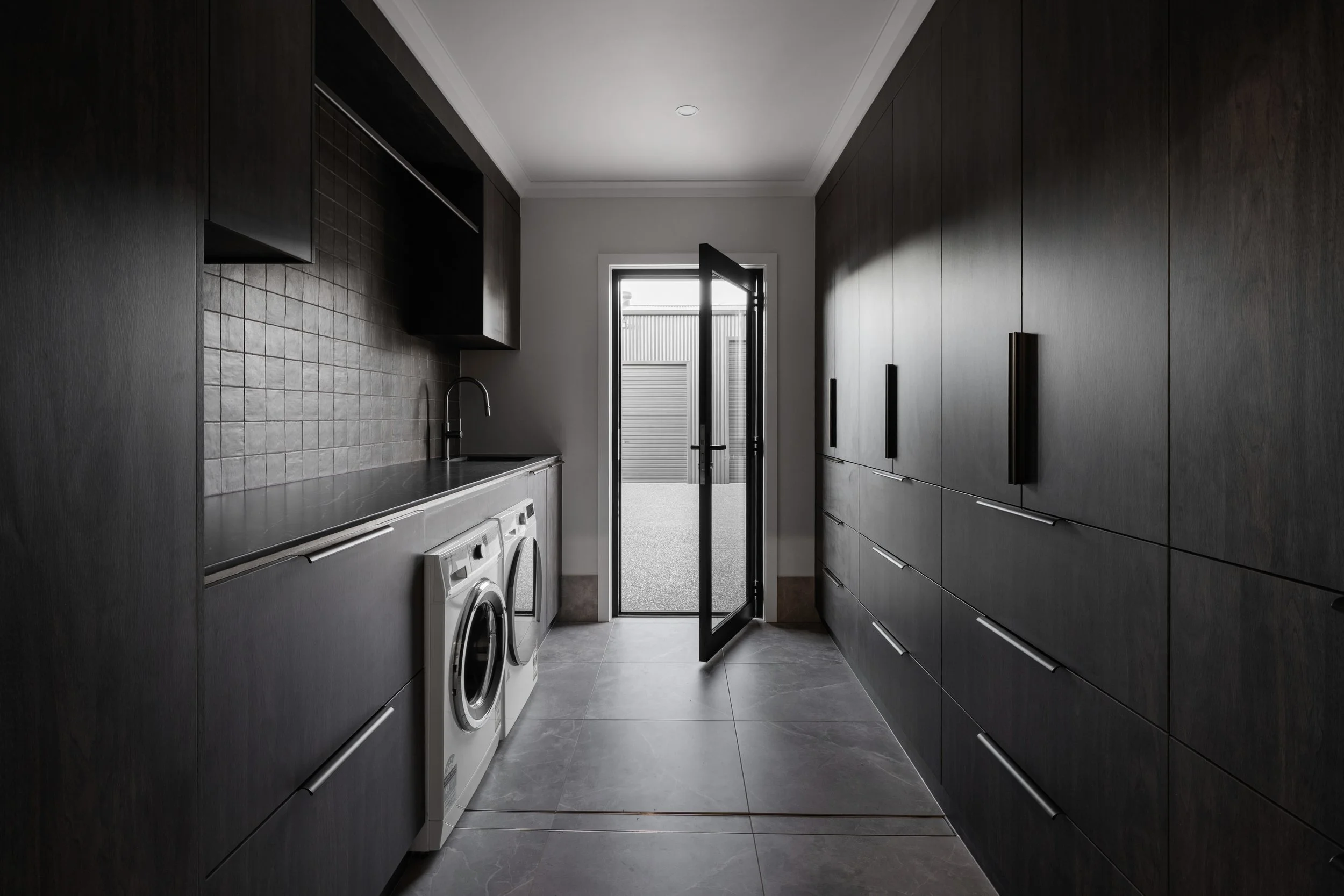 Modern laundry room with dark cabinetry, a washing machine, a sink, and a door leading outside.