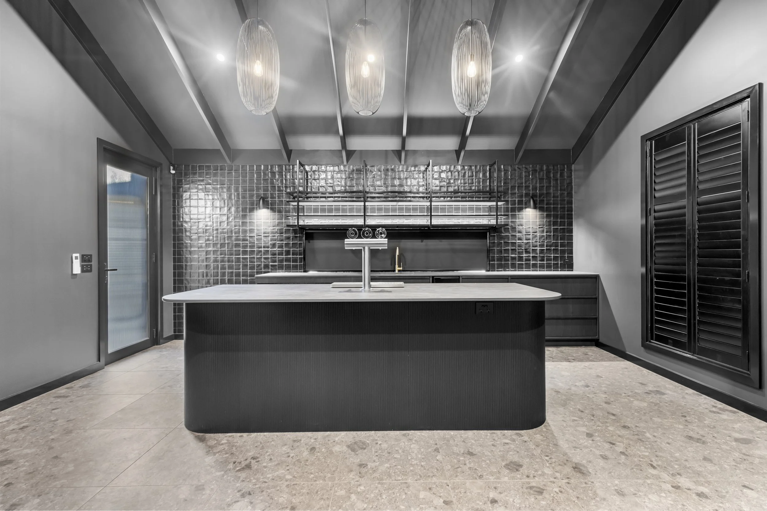 Modern kitchen with a black island, black cabinets, black shiplap backsplash, pendant lights, and hardwood floors.