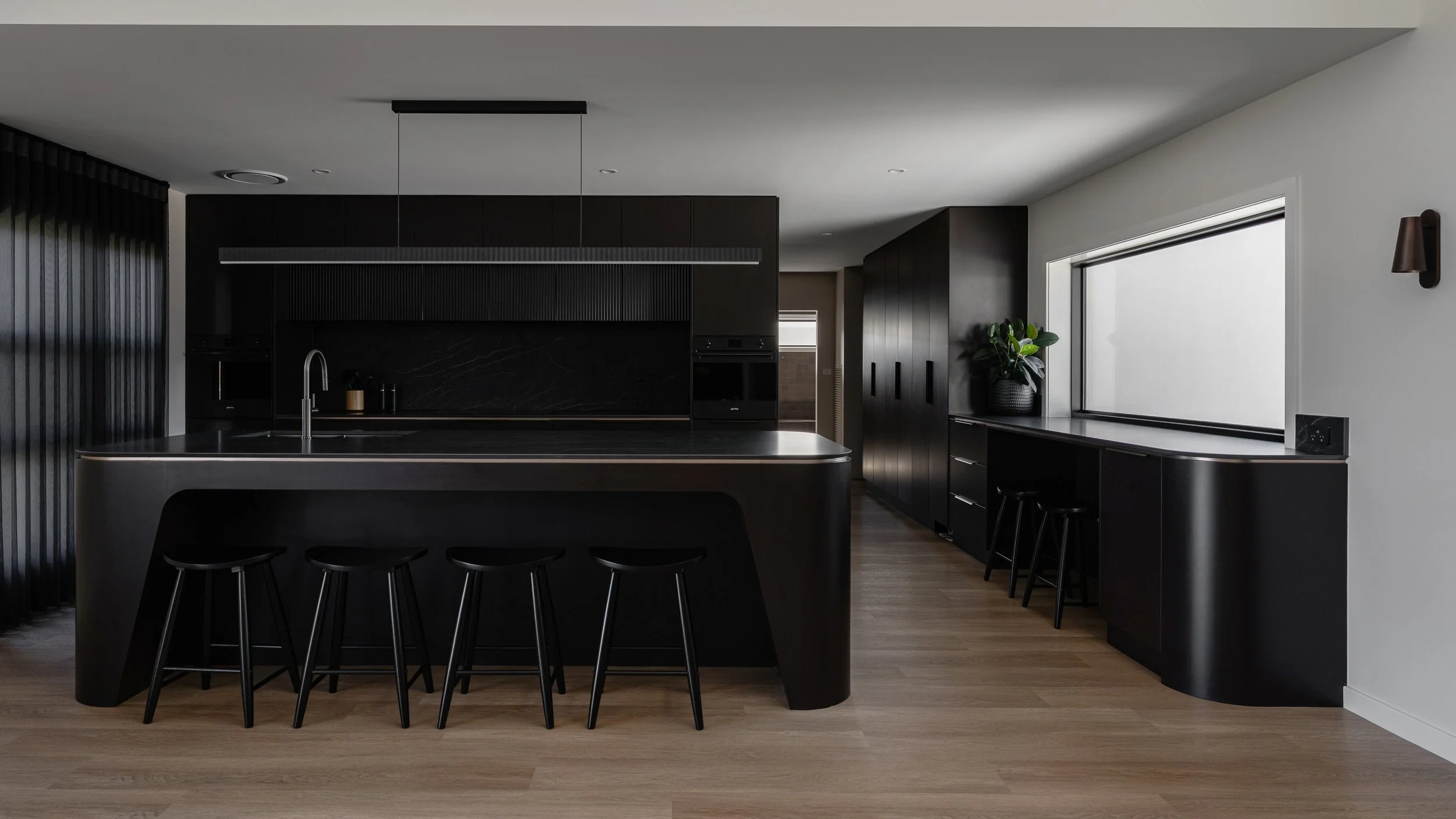 Modern black and gray kitchen with island, black stools, and a large window with a plant on the windowsill.