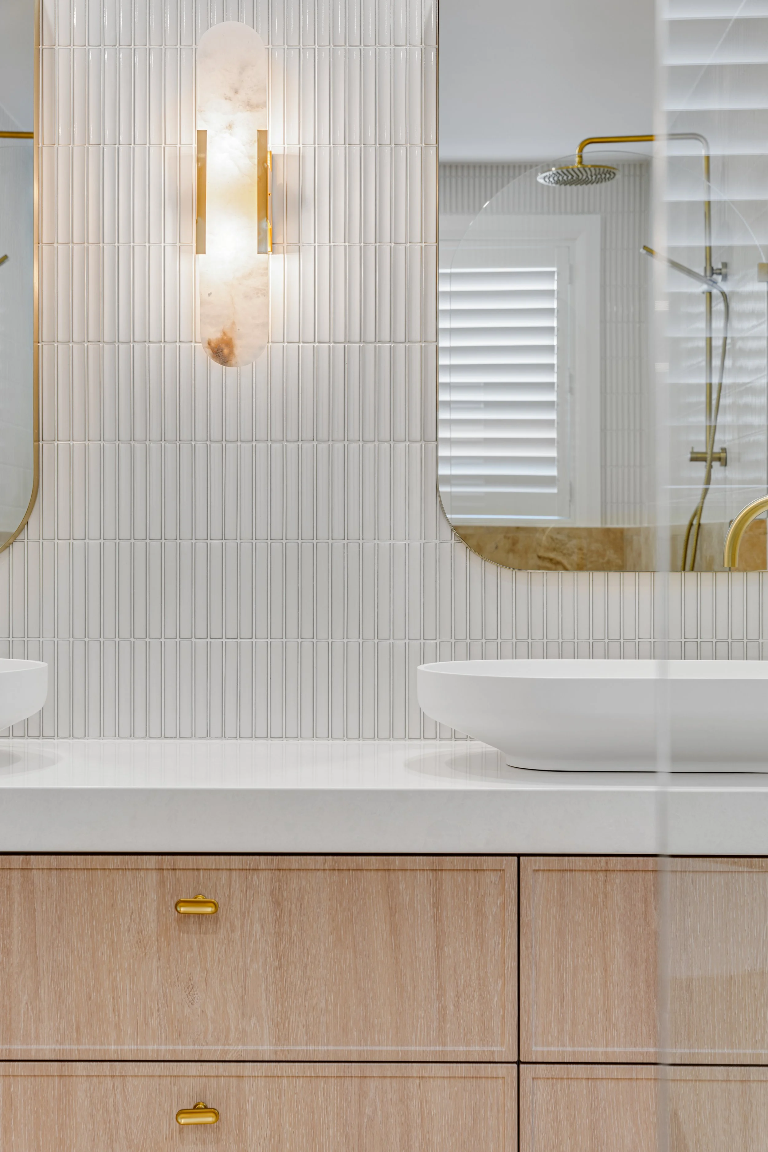 Bathroom with beige wooden cabinets, white sink, mirror, and walk-in shower with a rain shower head and white tile wall.