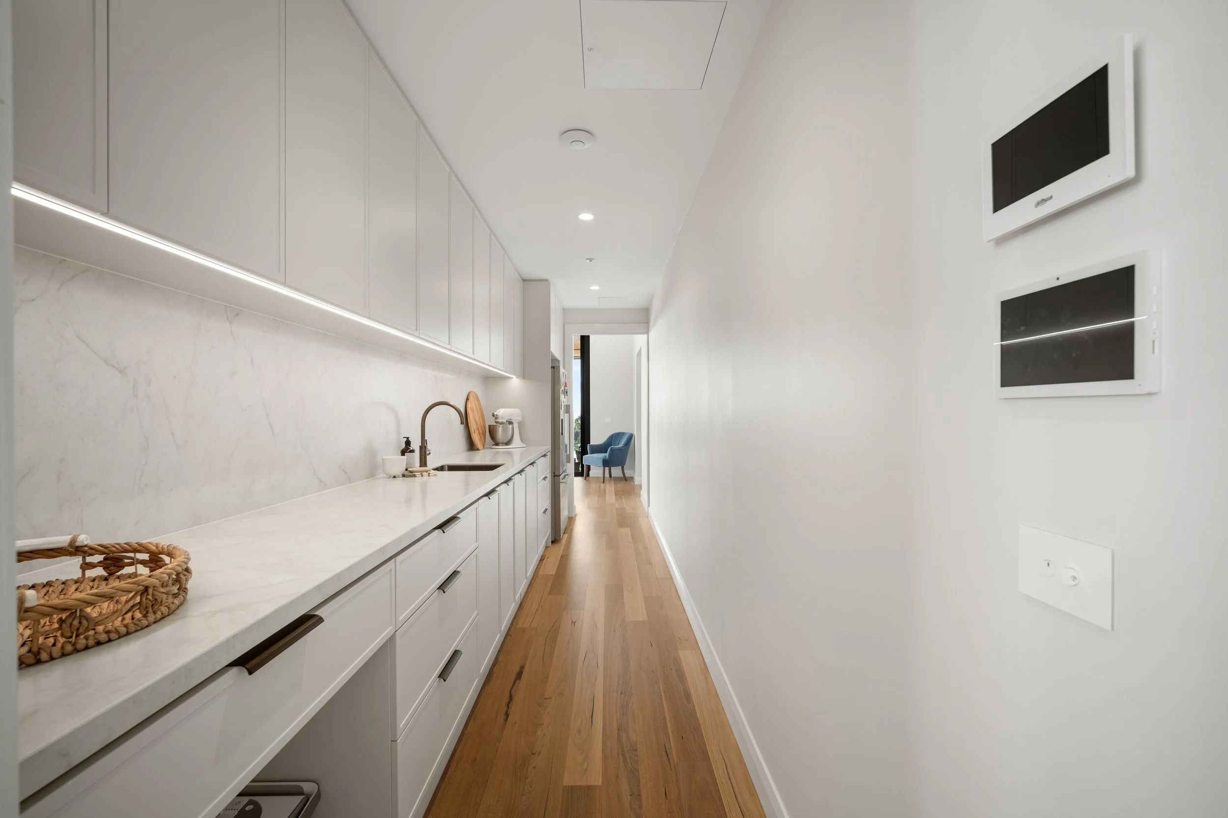 Modern kitchen with white cabinets, marble countertop, wooden floor, and wall-mounted screens.