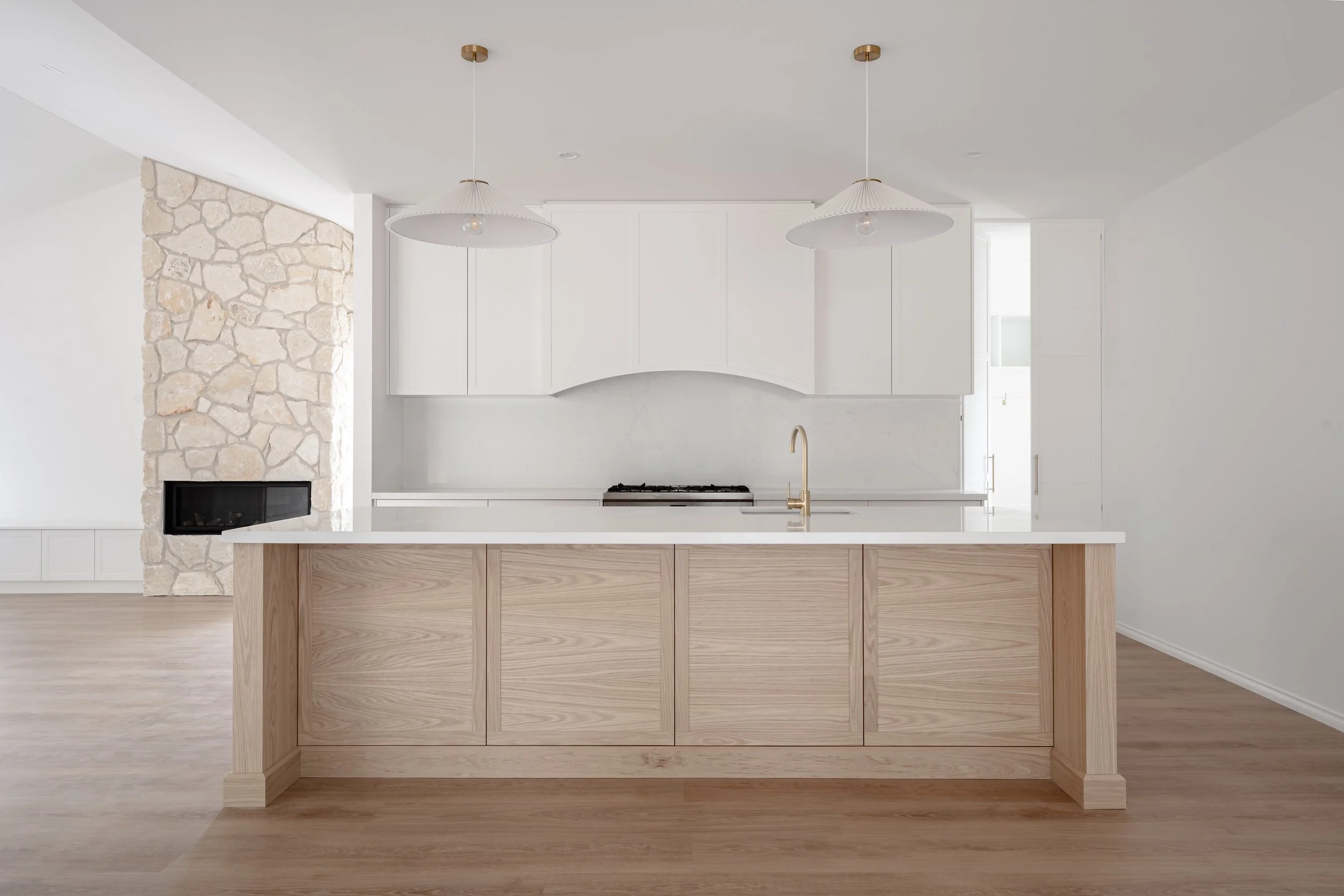 Modern kitchen with a white marble backsplash, white cabinets, a central island with a light wood finish, and two pendant lights hanging from the ceiling.