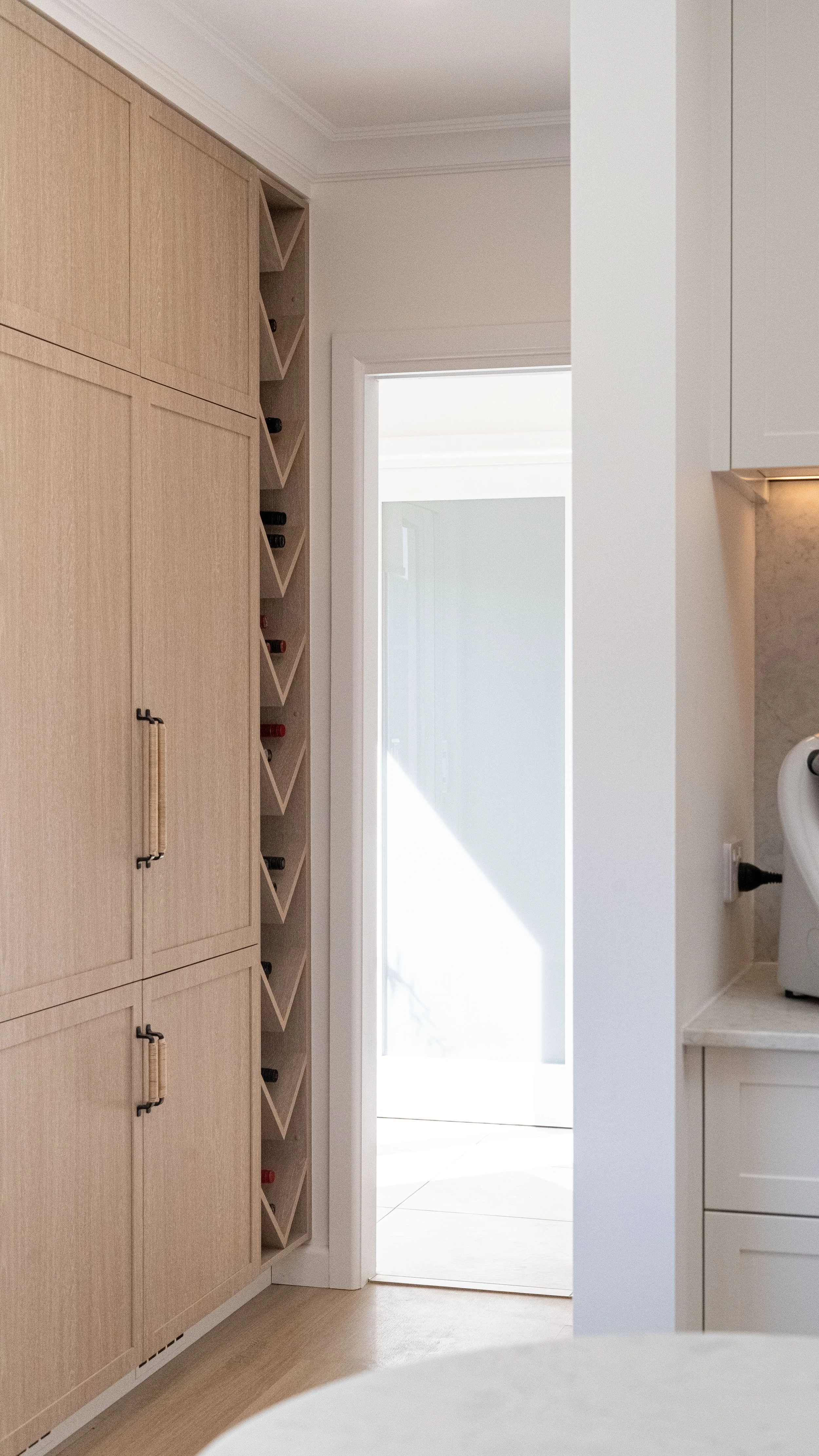 A doorway leading to a bright outdoor space, with a partial view of a light-colored kitchen cabinet on the right and wine storage compartments on the left.