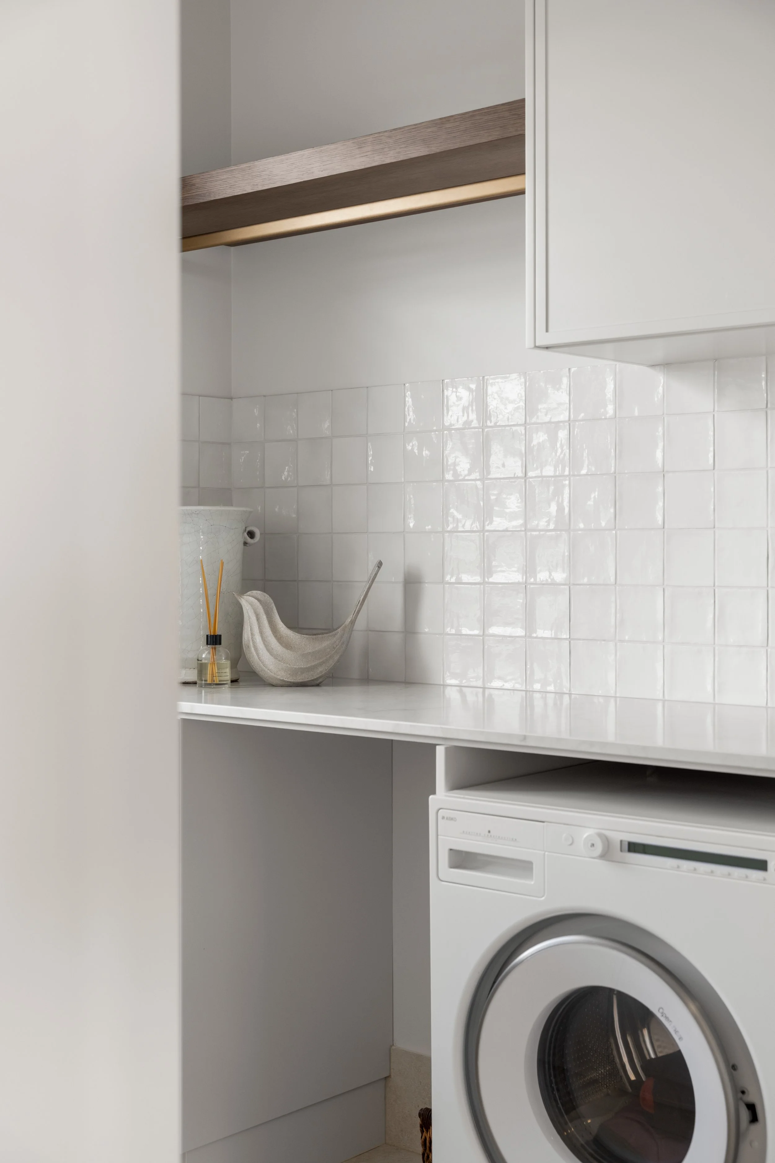 A laundry room with white cabinets, a white washing machine, a countertop, and wall tiles. There is a small decorative soap dispenser and reed diffuser on the counter.