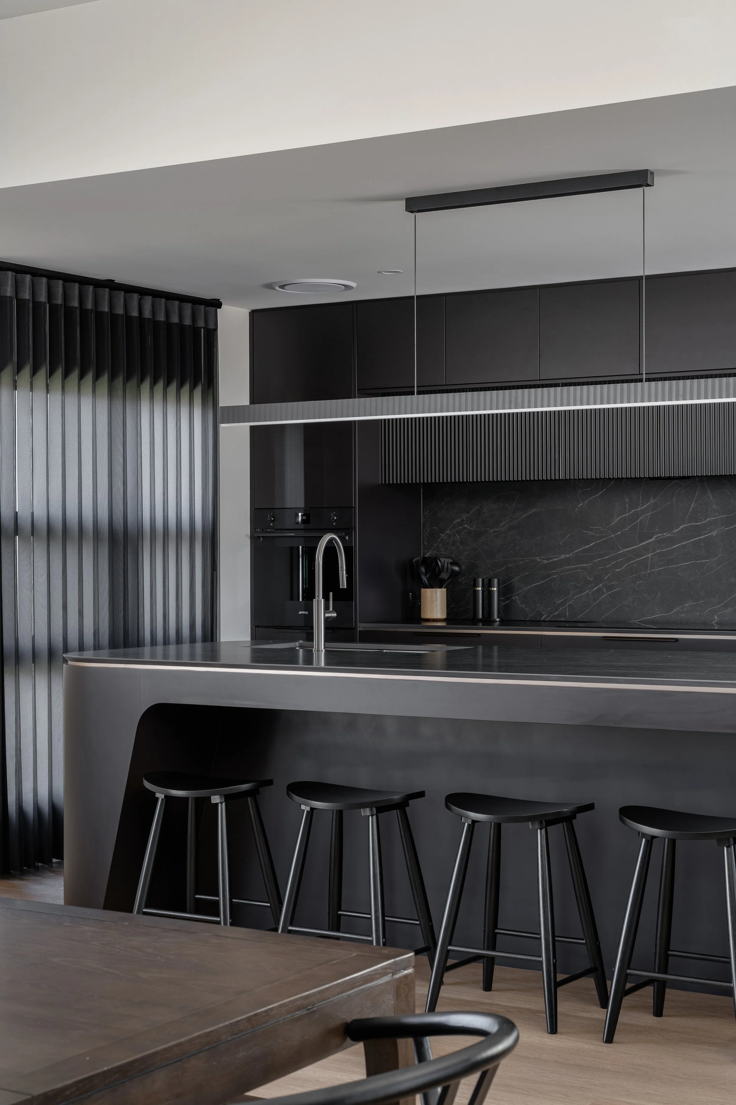 Modern kitchen with black cabinets, a dark marble backsplash, a countertop island with bar stools, and minimalistic lighting.