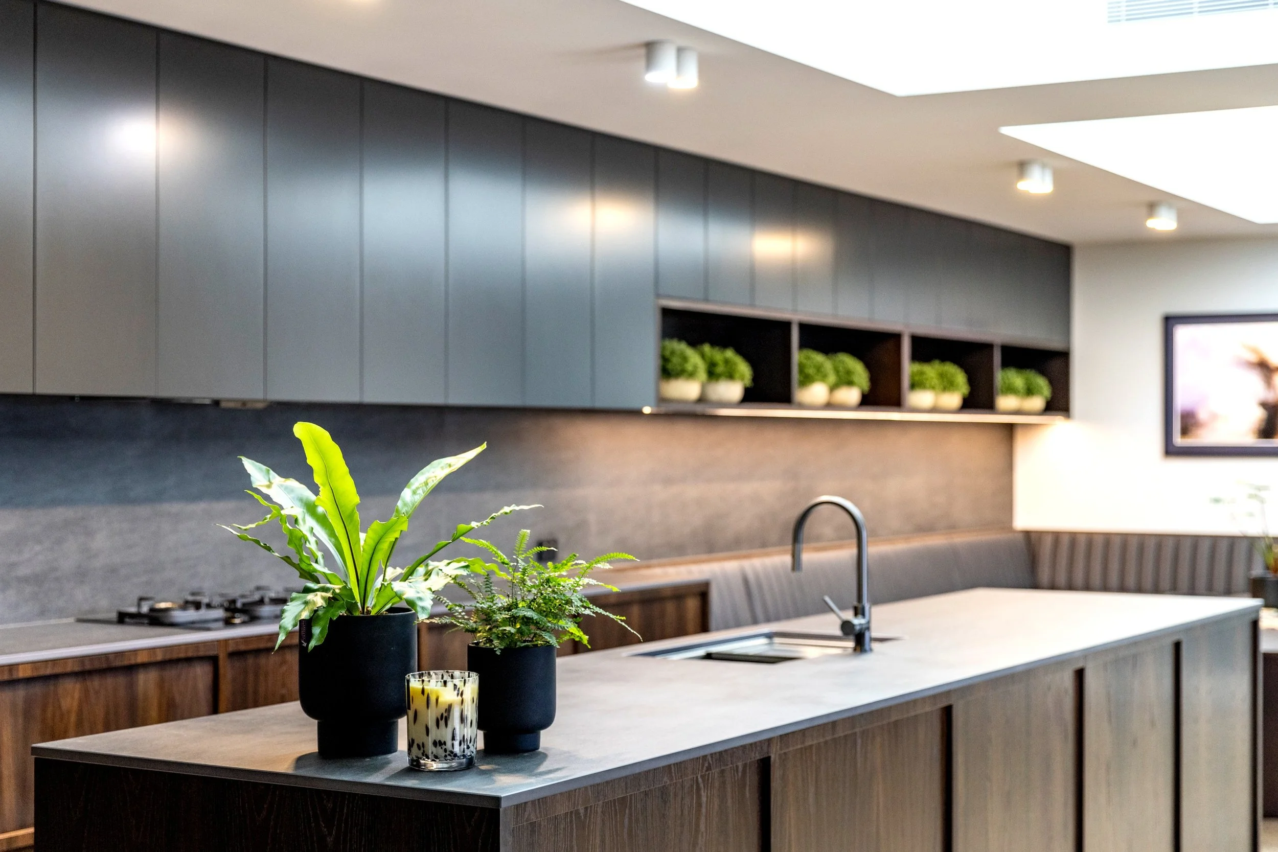 A modern kitchen with dark wood cabinets, a countertop with potted plants, and a bright ceiling with recessed lighting.