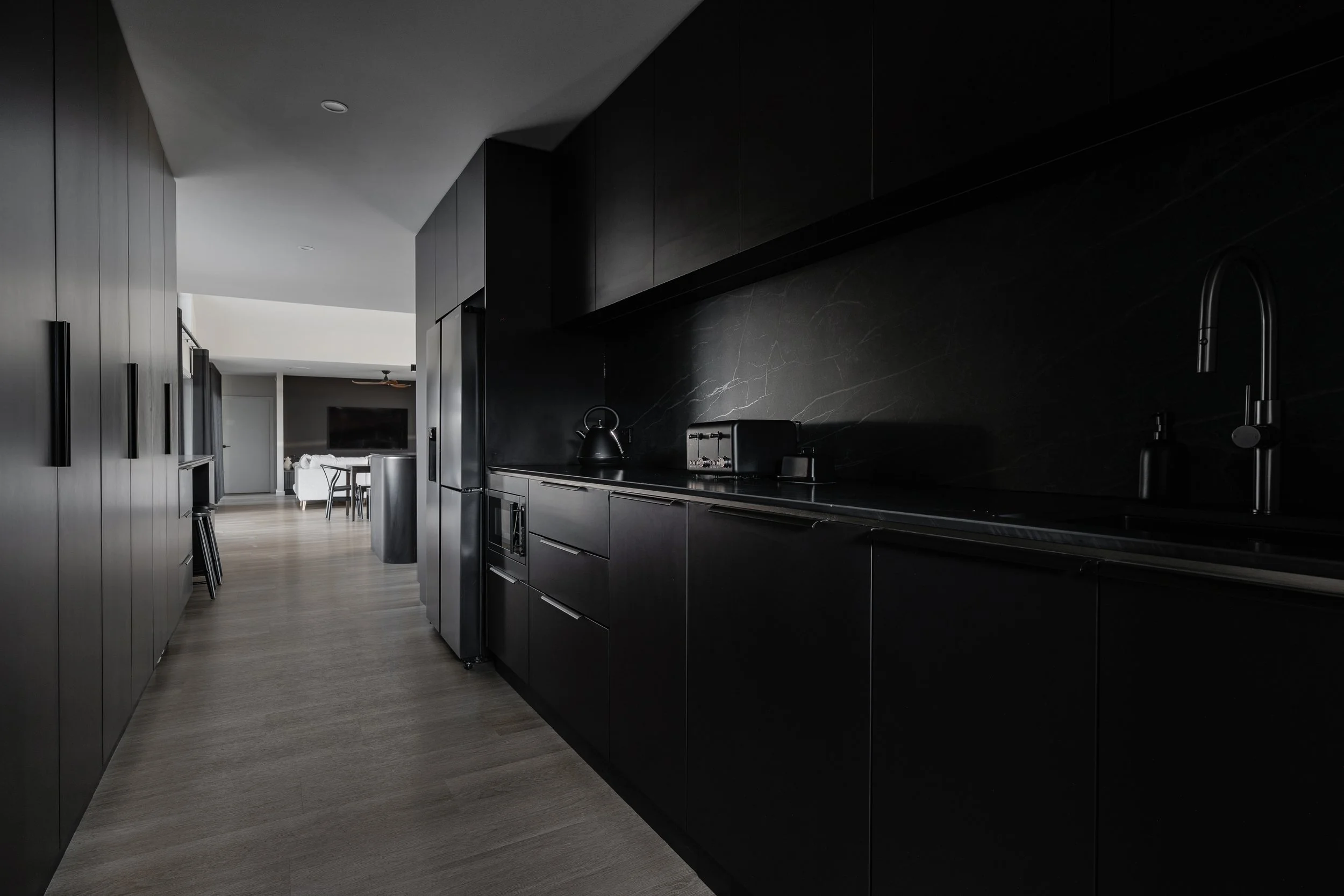Modern kitchen with black cabinets, dark marble backsplash, wooden floor, and minimalistic design.