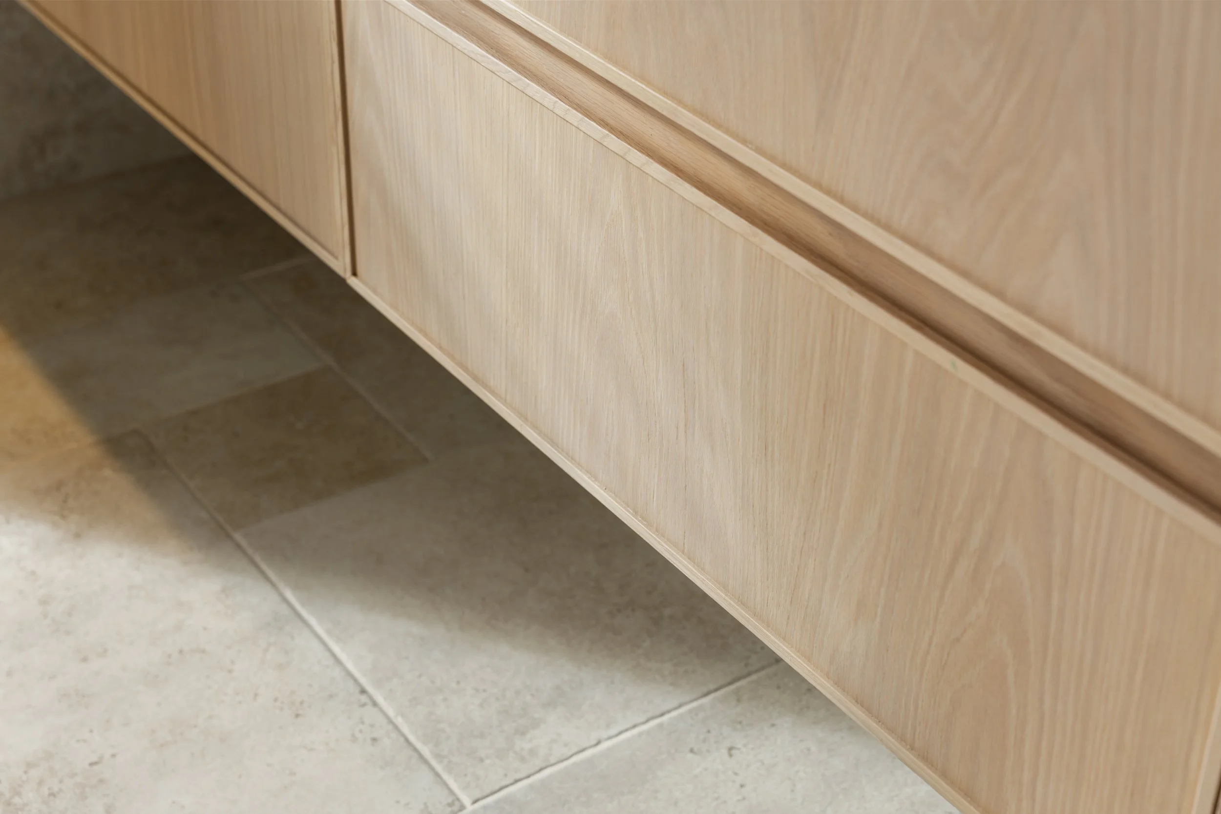 Close-up of the lower part of a wooden cabinet with a curved detail on the bottom edge, near tiled flooring.