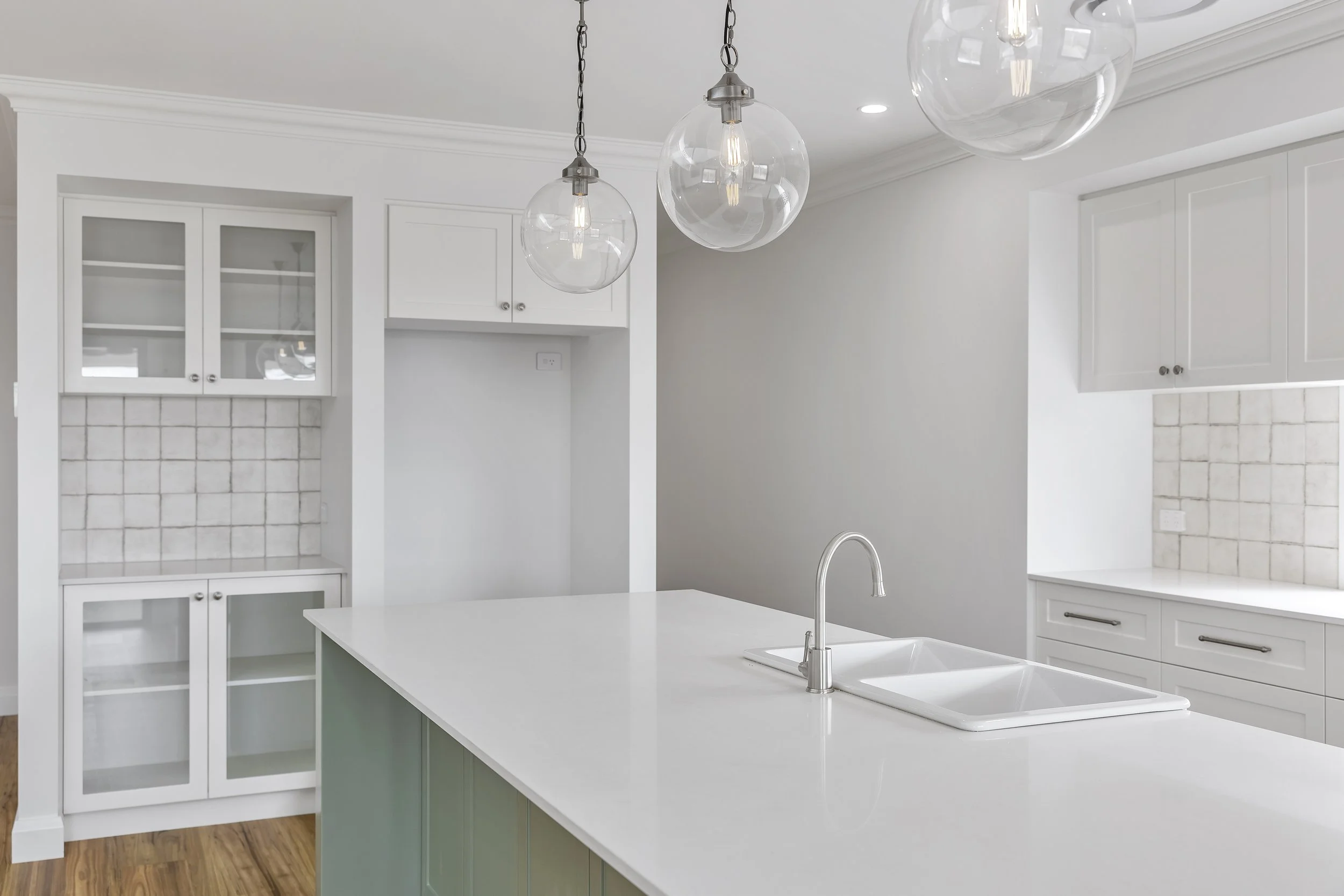 Modern kitchen with white cabinets, a white island with a sink, a light-colored tile backsplash, and three glass globe pendant lights hanging from the ceiling.