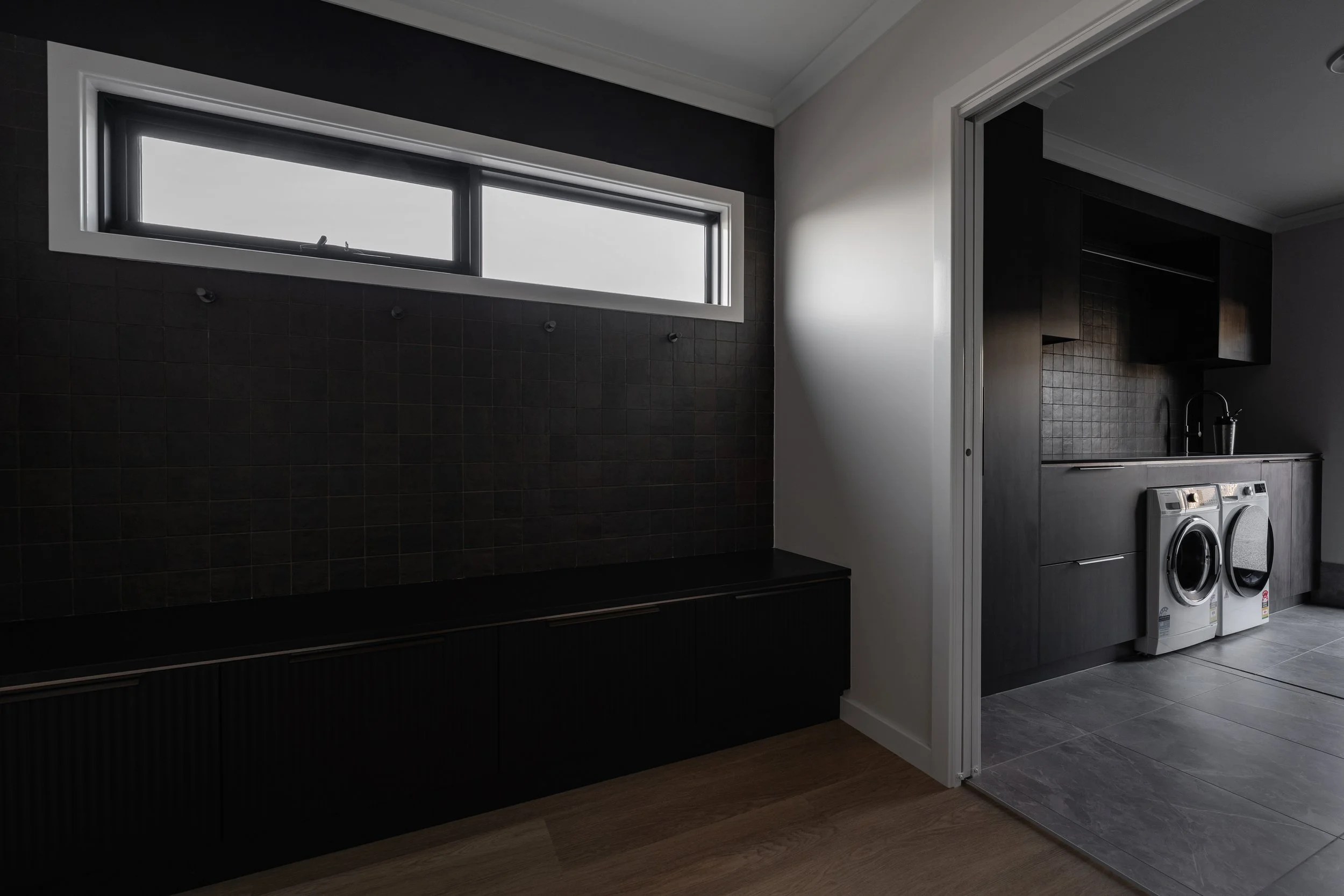 A laundry room with black tiled wall, a small window, gray cabinets, and a washer and dryer.