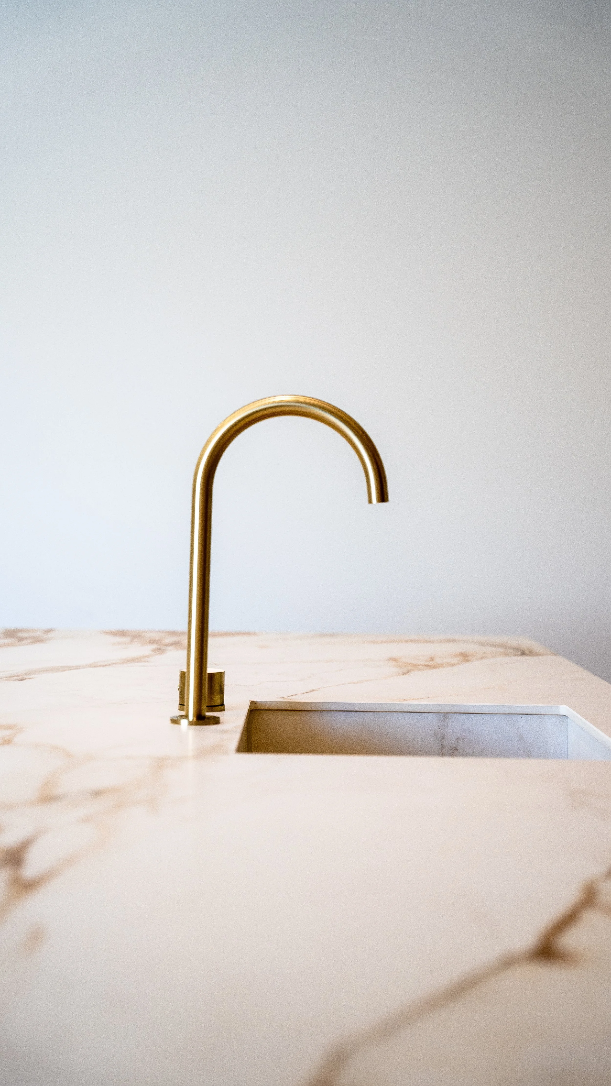 Close-up of a modern gold kitchen faucet above a marble countertop with a white sink.