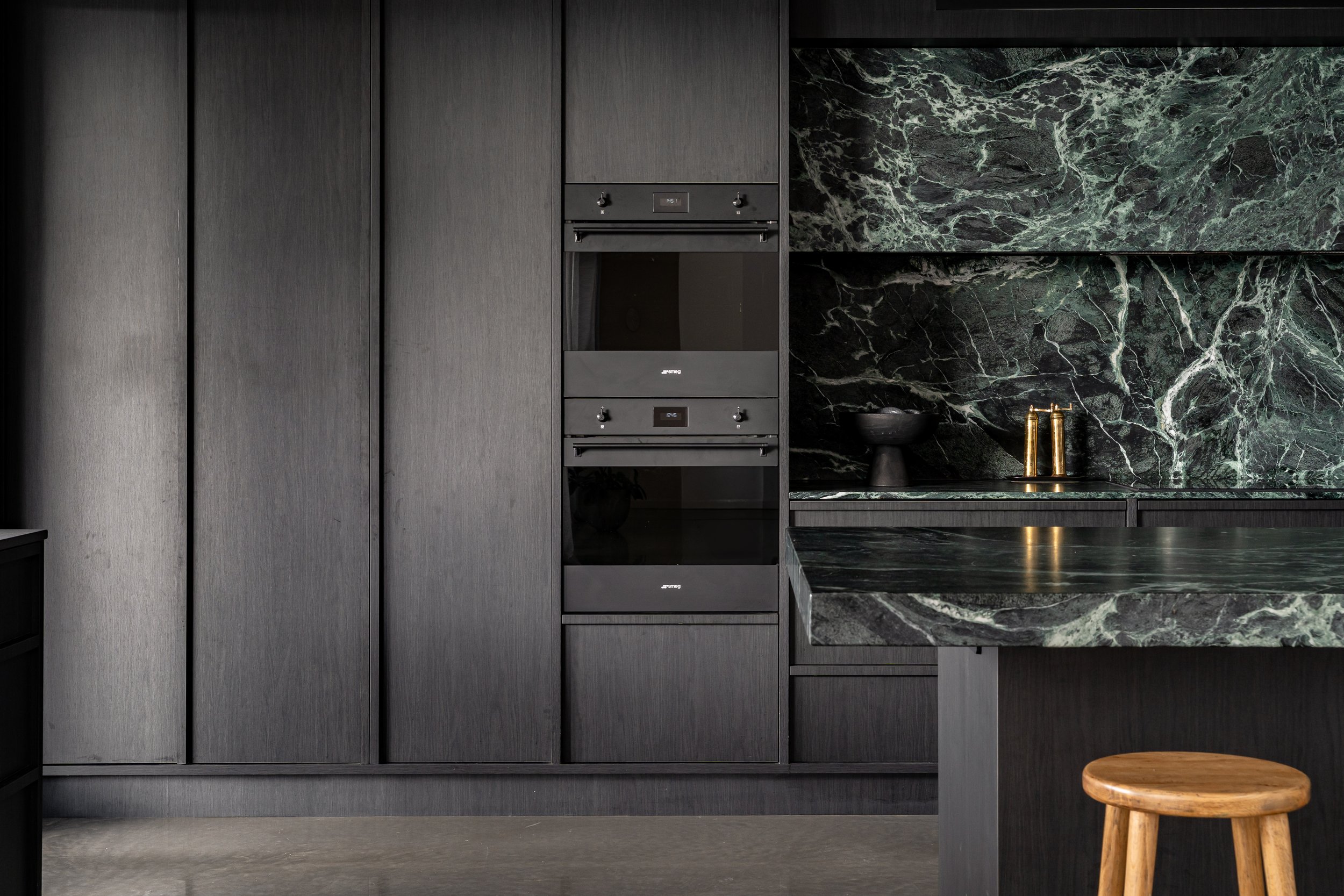 A modern kitchen with dark wood cabinets, a black oven, and green marble countertops and backsplash.