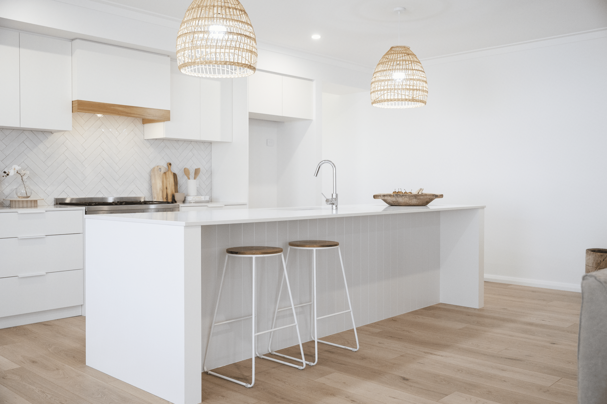 Modern kitchen with white cabinets, wood accents, wicker pendant lights, and a white island with stools.