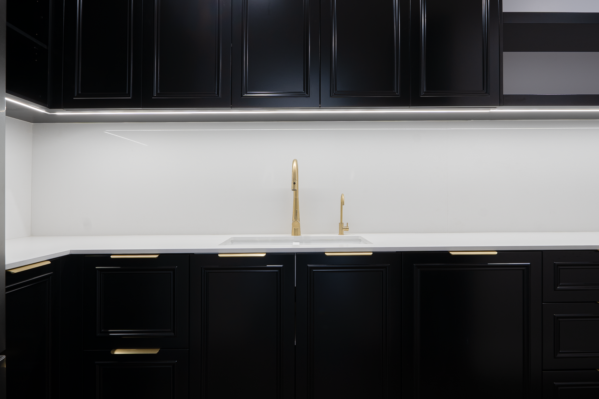 Modern kitchen with black cabinets, white countertop, gold sink faucet, and under-cabinet lighting.
