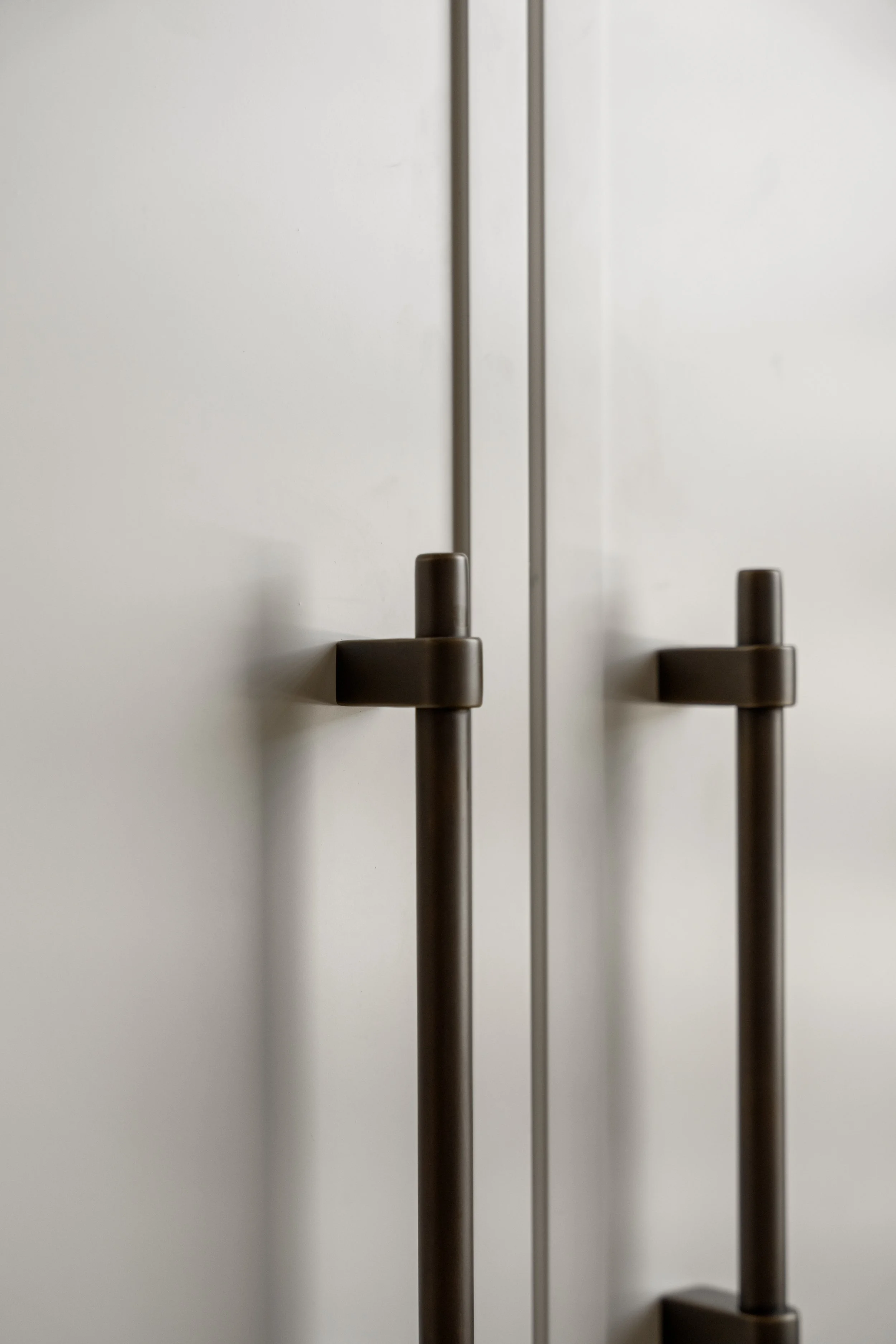 Close-up of two modern, metallic door handles on a plain white door, positioned vertically and reflecting light.
