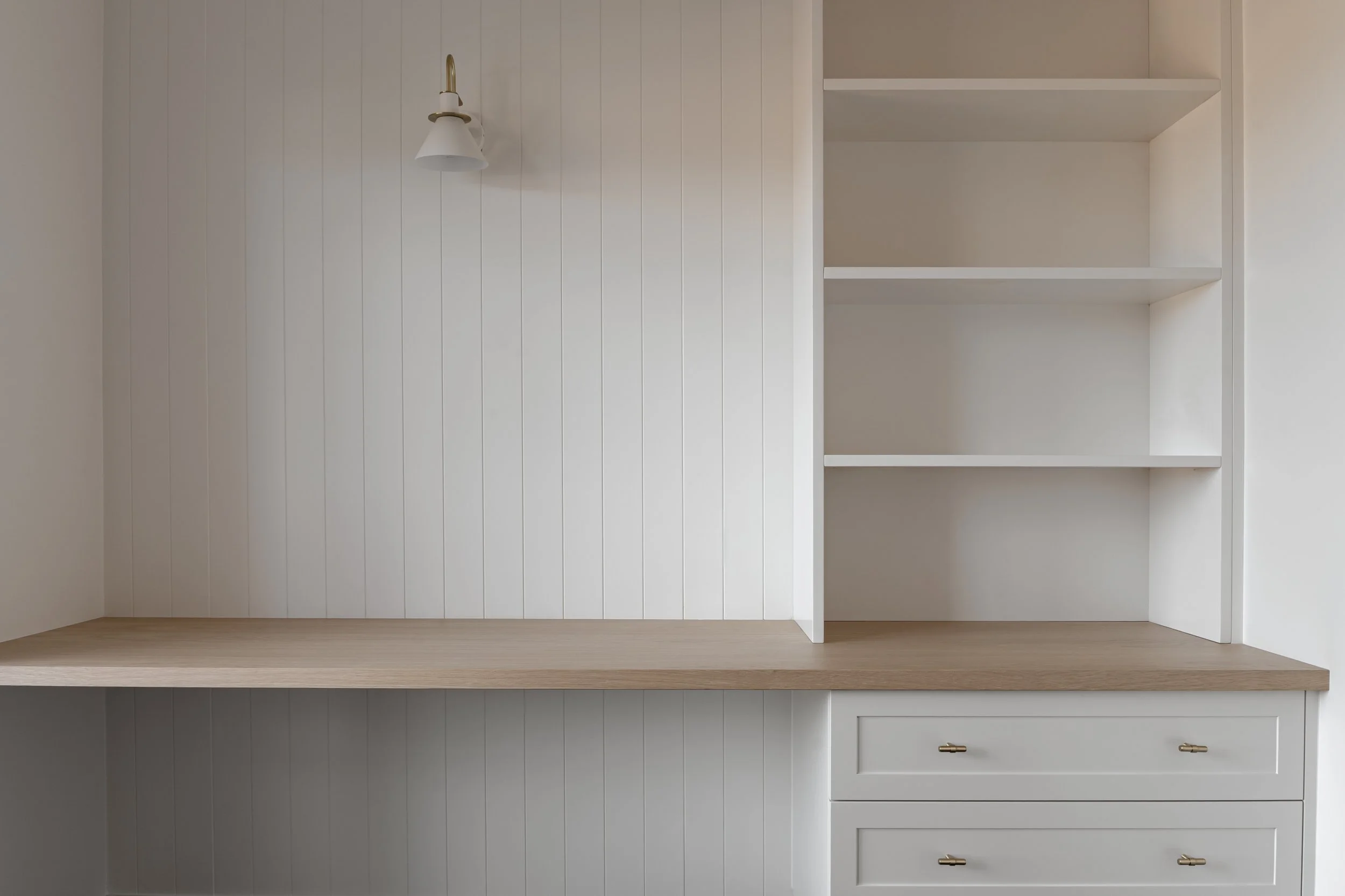 Empty white kitchen cabinet with a wooden countertop and gold cabinet handles.