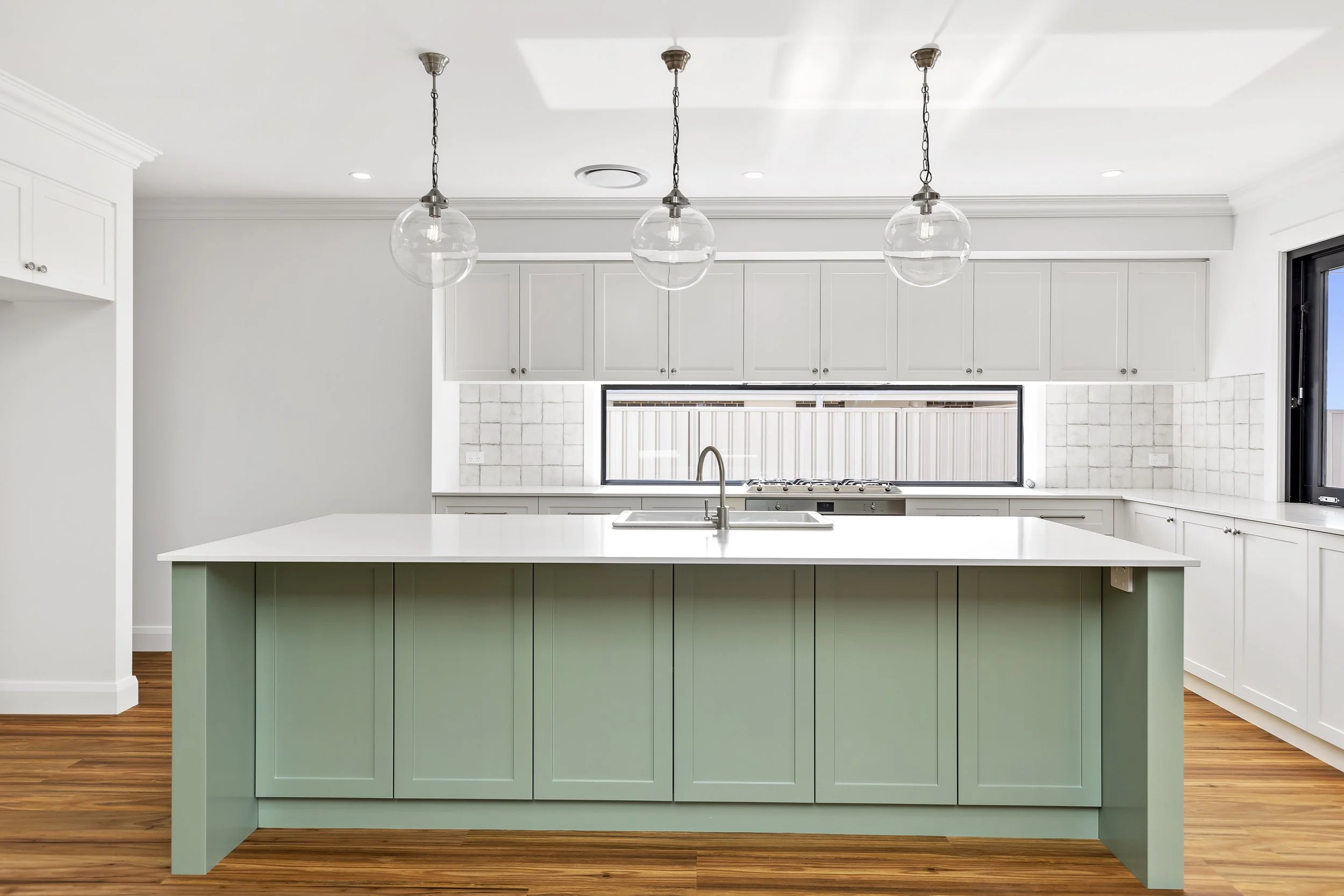 Modern kitchen with white cabinets, a green central island, a white countertop, and three clear glass pendant lights hanging from the ceiling.