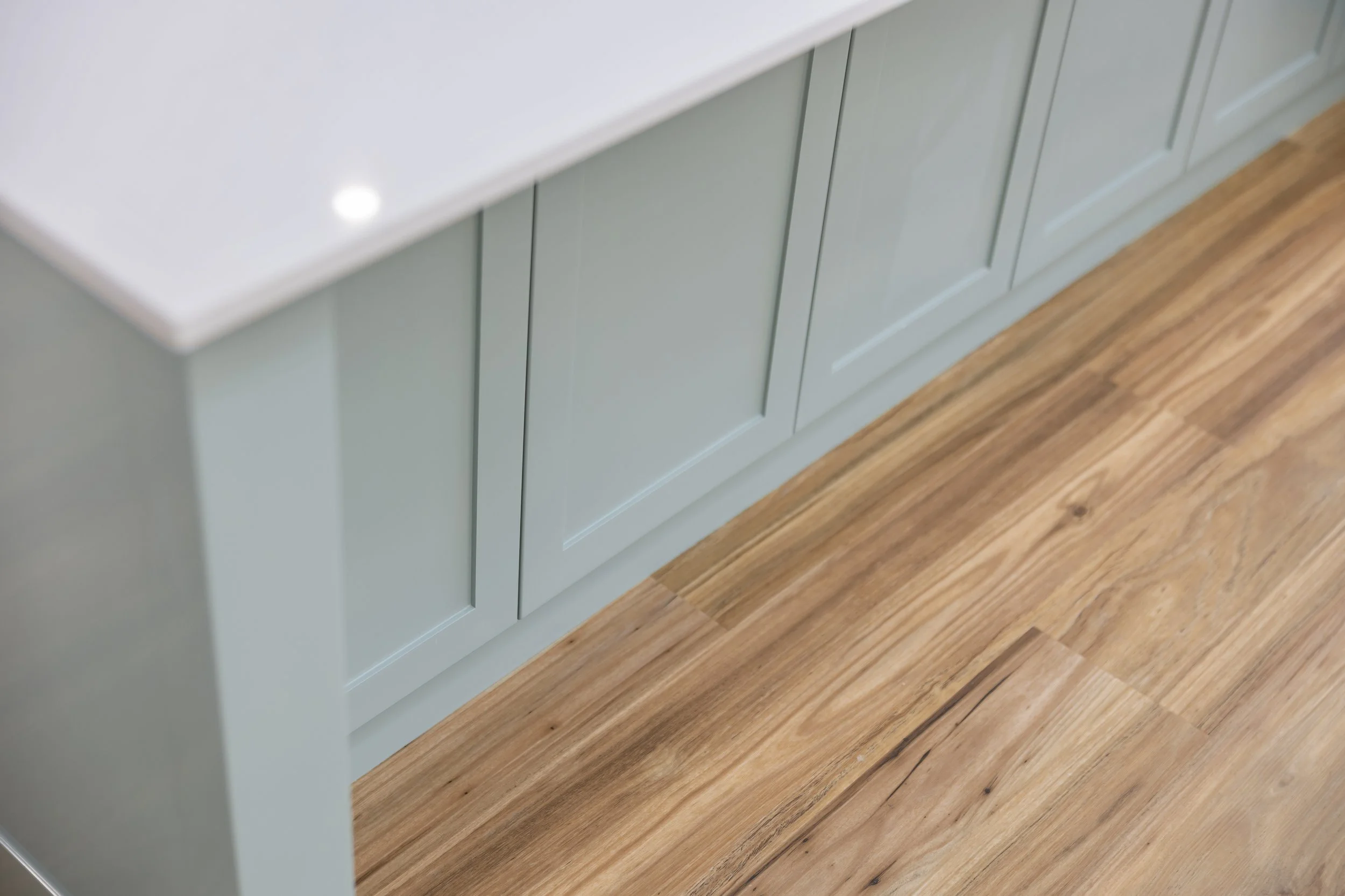 Close-up of a light green kitchen cabinet with a white countertop and wooden floor.