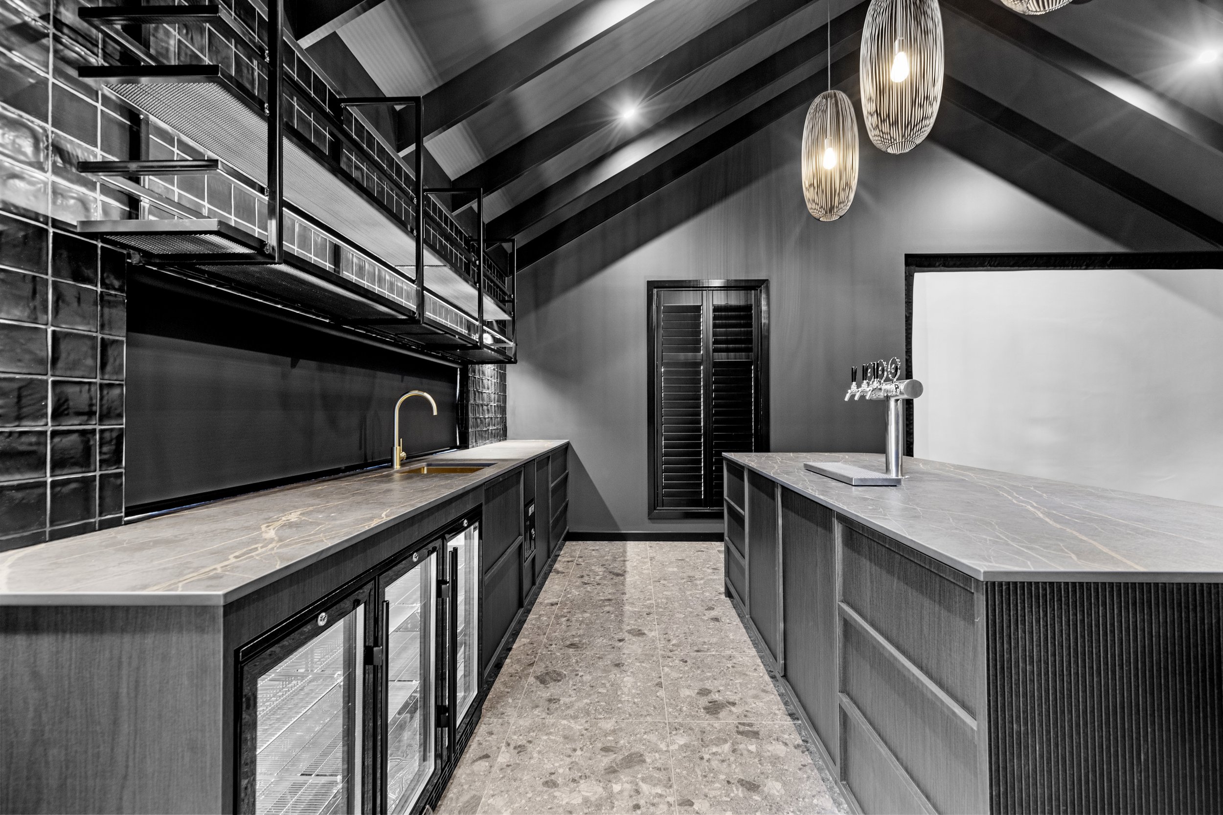 Modern kitchen with dark cabinets, a marble countertop, a sink with a gold faucet, black tile backsplash, and pendant lights hanging from a sloped ceiling.