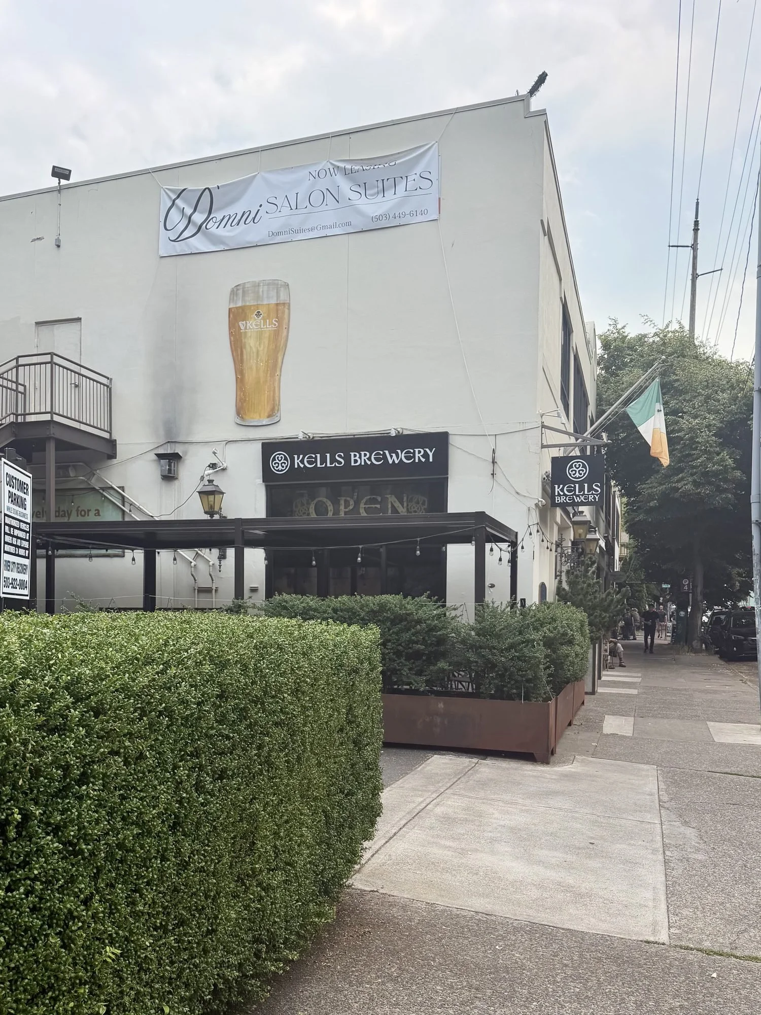 two-story cream building containing a brewery behind a short shrub and an awning