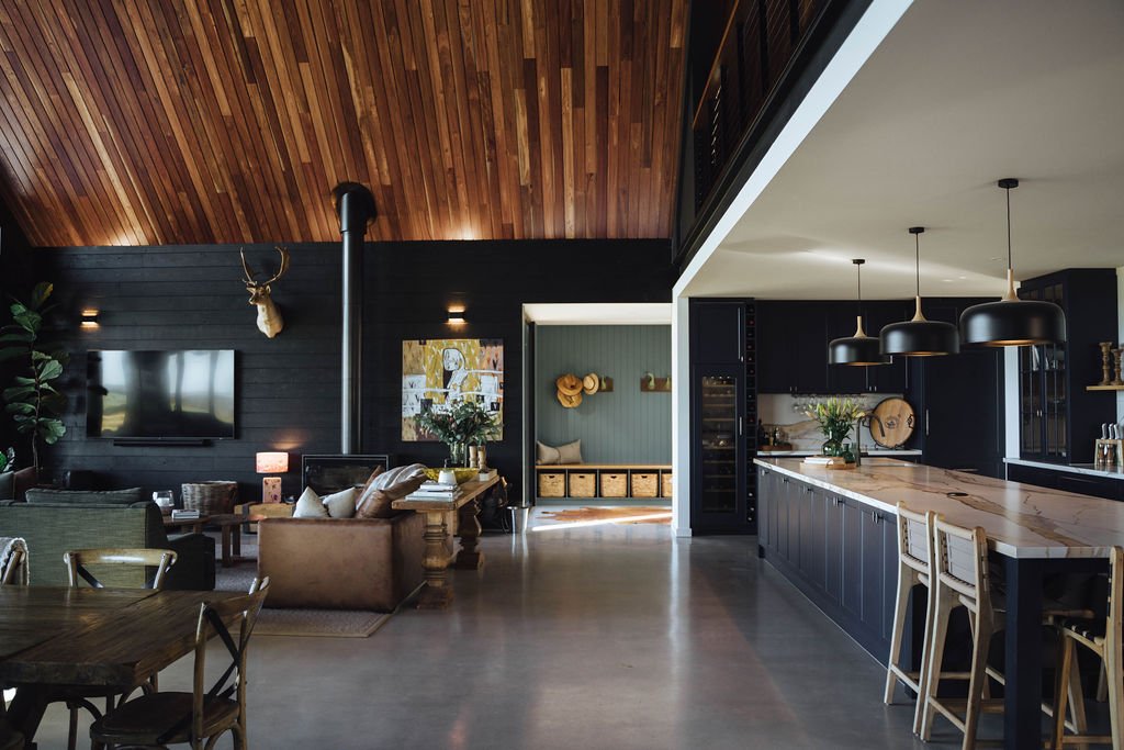 Open-concept living room and kitchen with dark cabinetry, wooden ceiling, and modern decor.