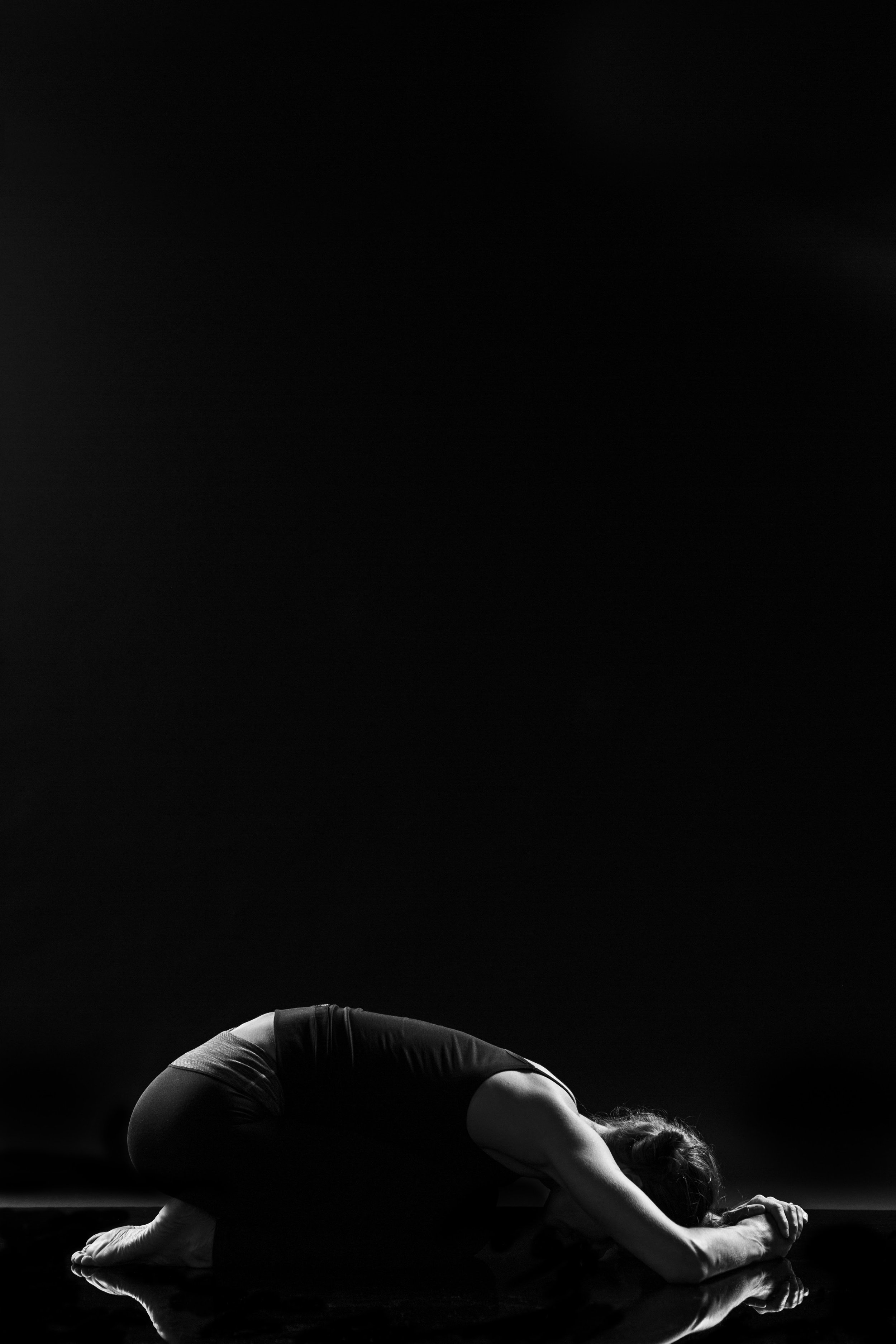Amanda Ferris practicing yoga in a child's pose on a dark background, with their arms extended forward and their head resting on the ground.