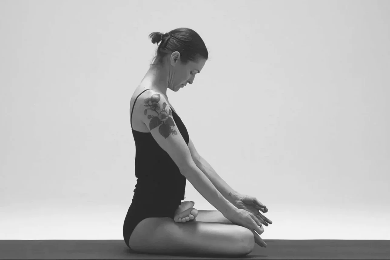 A woman practicing yoga in padmasana on a yoga mat, against a plain light background.