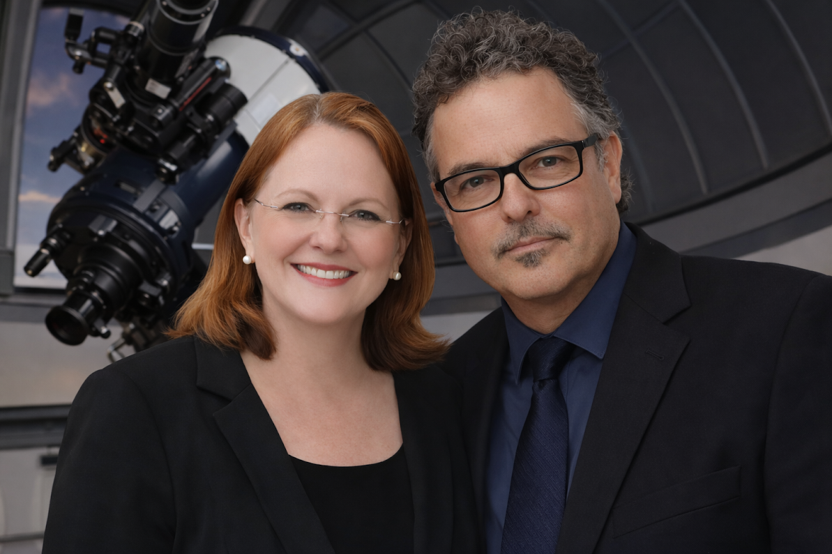 A smiling woman with red hair and glasses, and a serious man with curly gray hair and glasses, both in professional attire, standing in front of an astronomical telescope inside a planetarium or observatory.