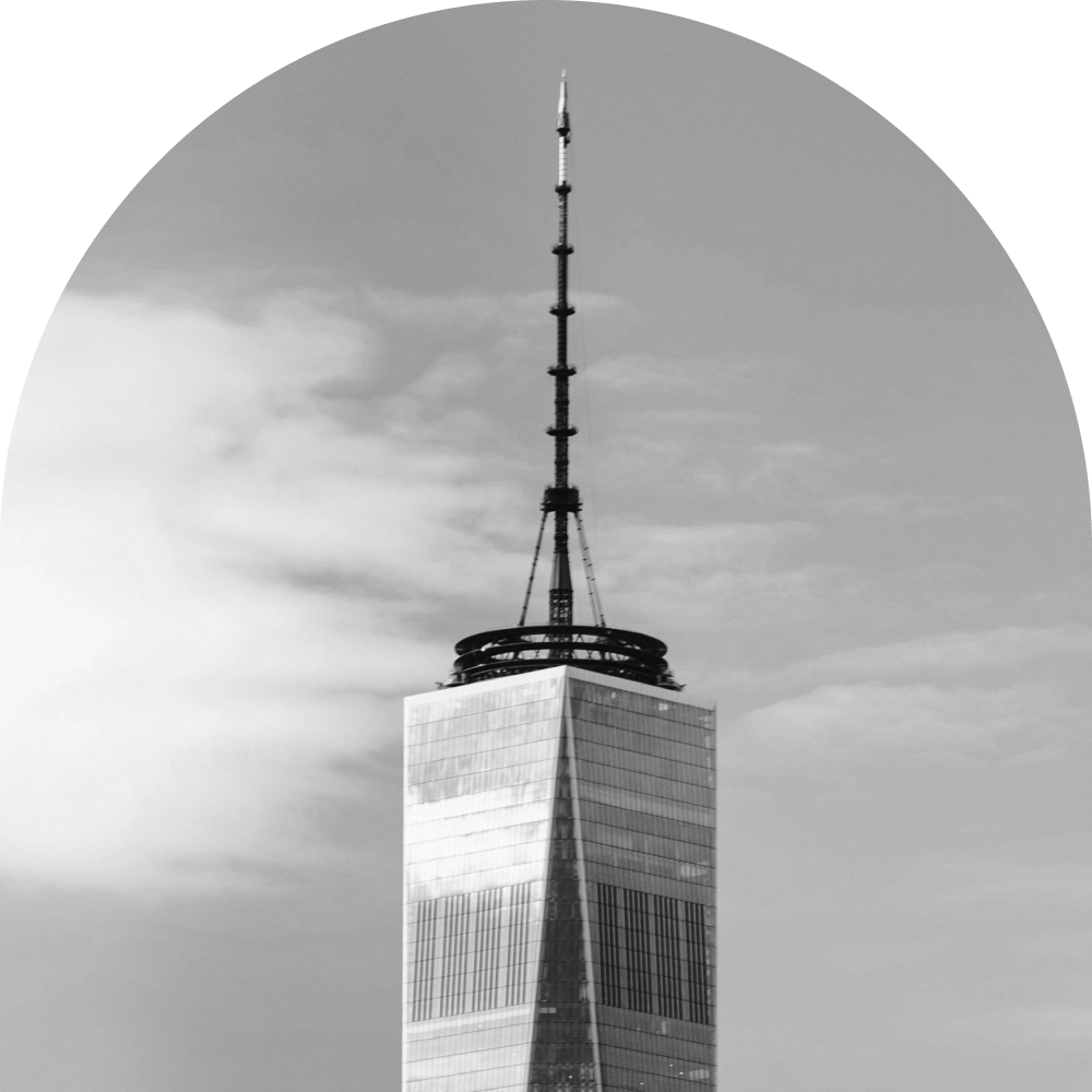 Black and white photo of the One World Trade Center with a cloudy sky in the background.