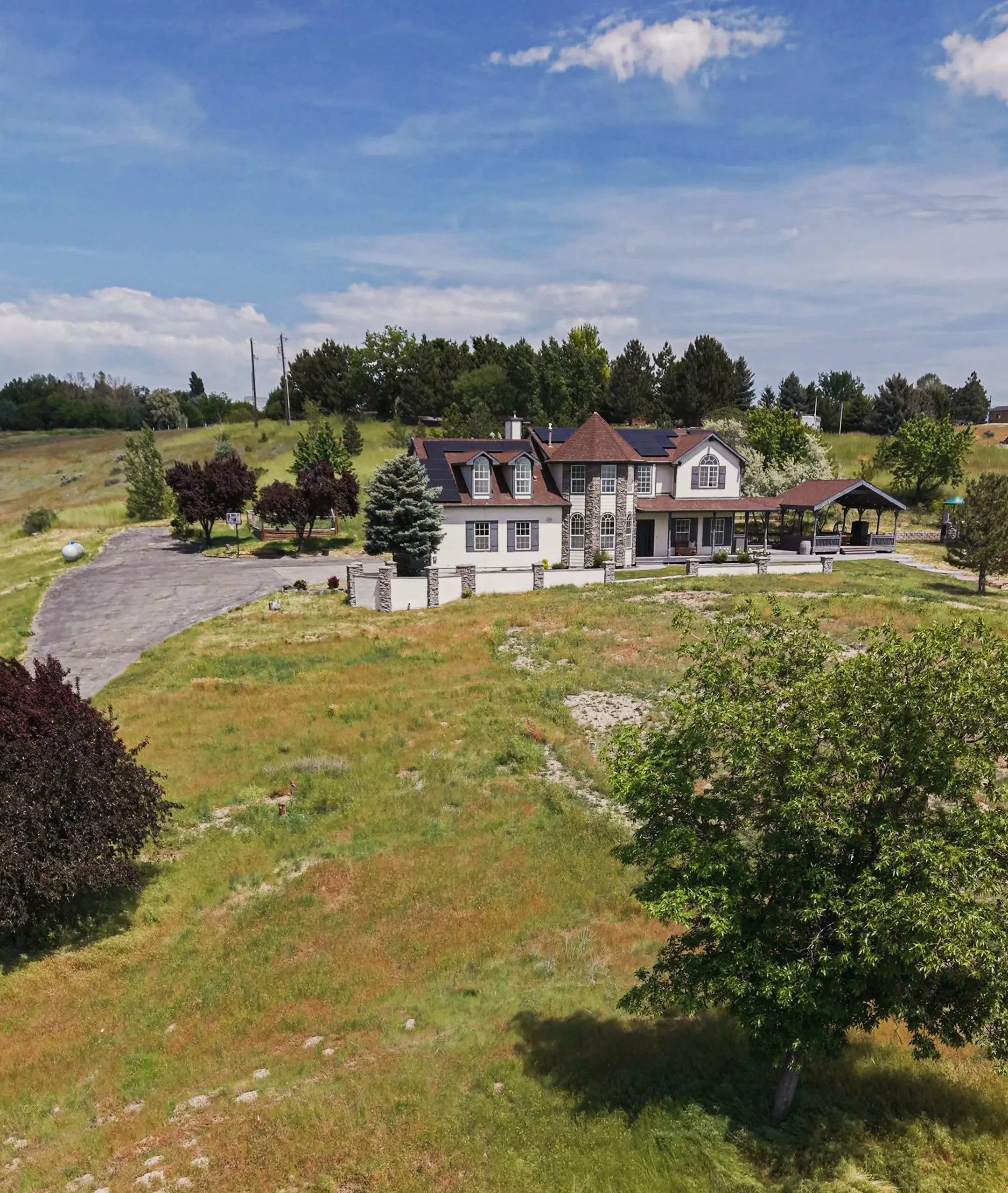 A large house with a yard full of trees and greenery, sitting in a semi-rural area under a partly cloudy sky.