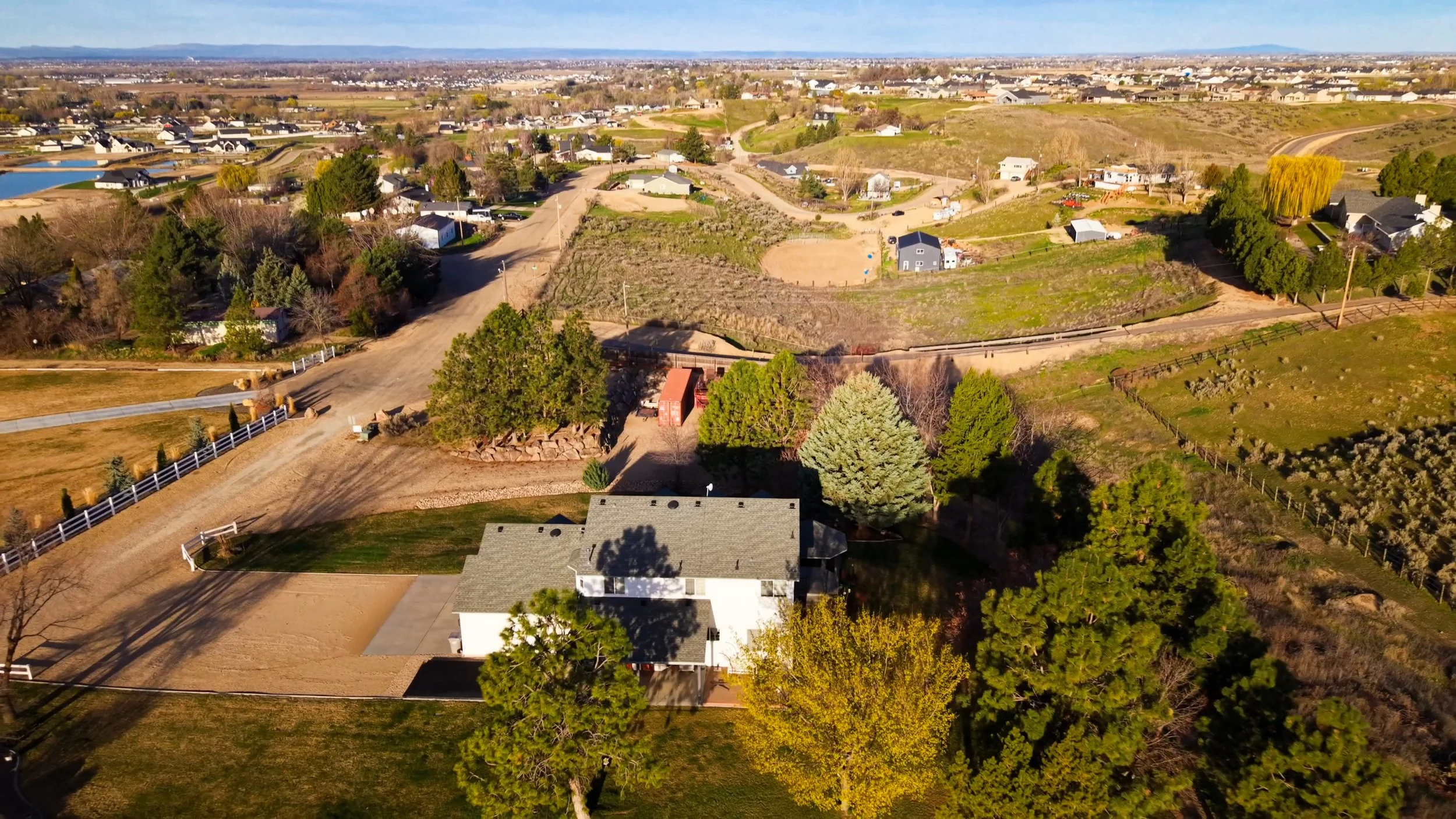 An aerial view of a suburban neighborhood with houses, trees, and open land, showing a mix of residential areas and natural scenery under a clear sky.