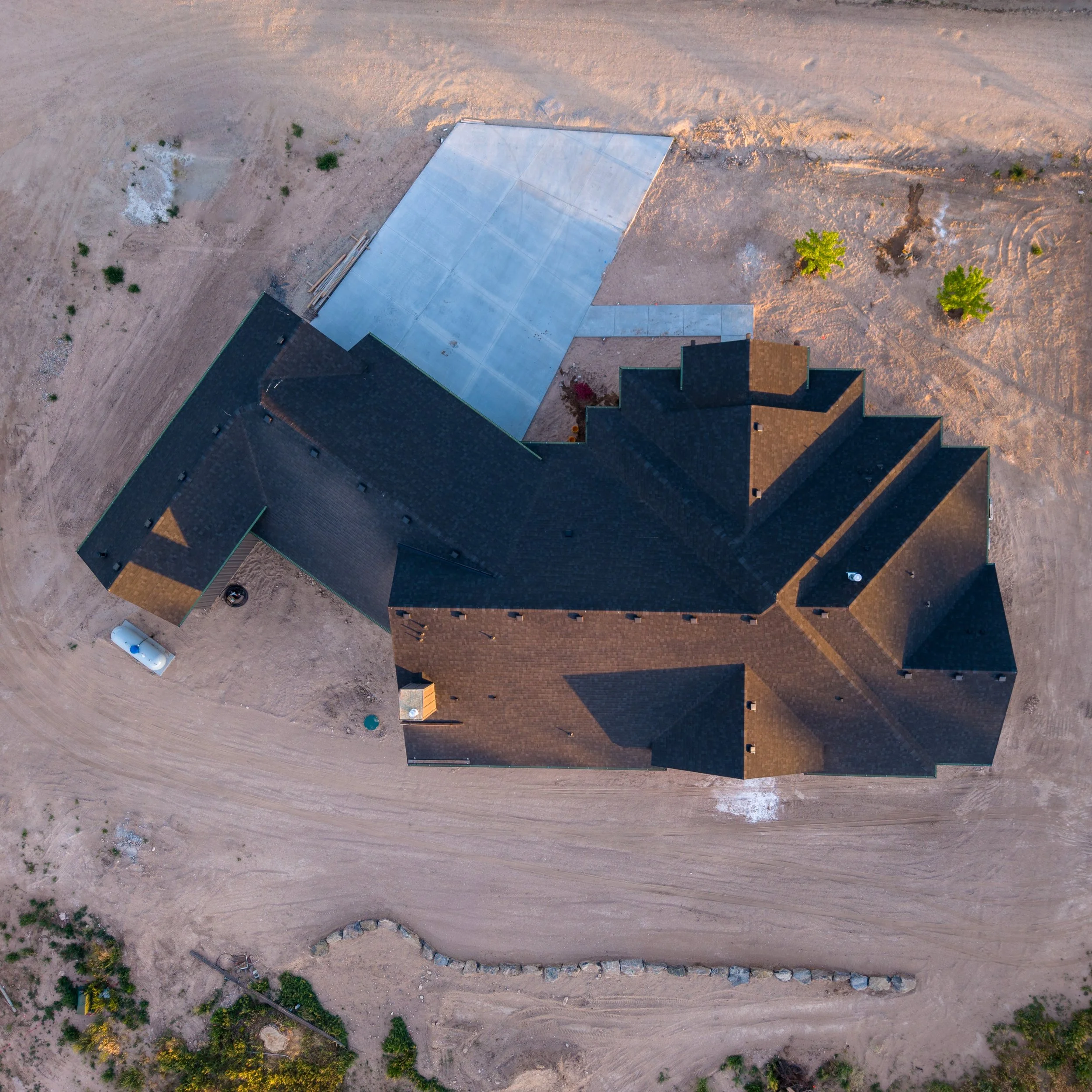 An aerial view of a house with a newly constructed concrete driveway in a desert-like area with sparse vegetation and trees.