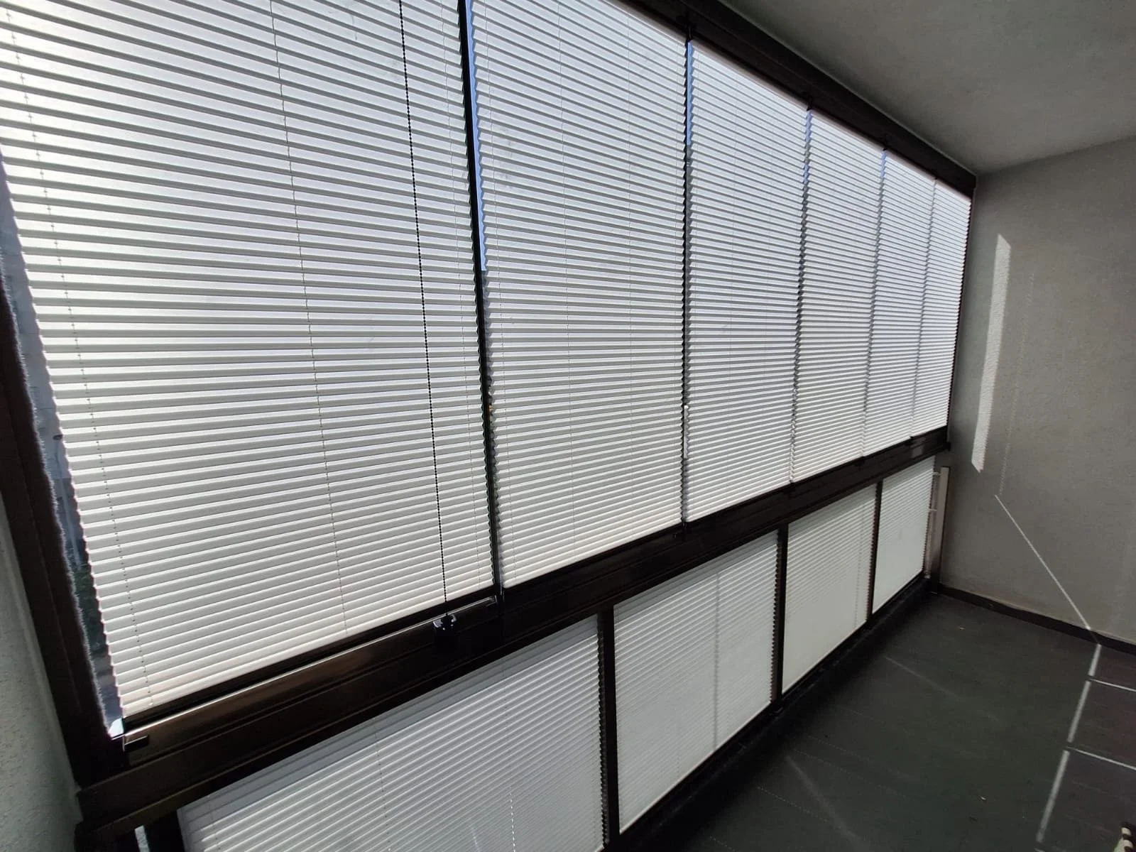 Window with closed white horizontal blinds and black frame, wall and tiled floor.
