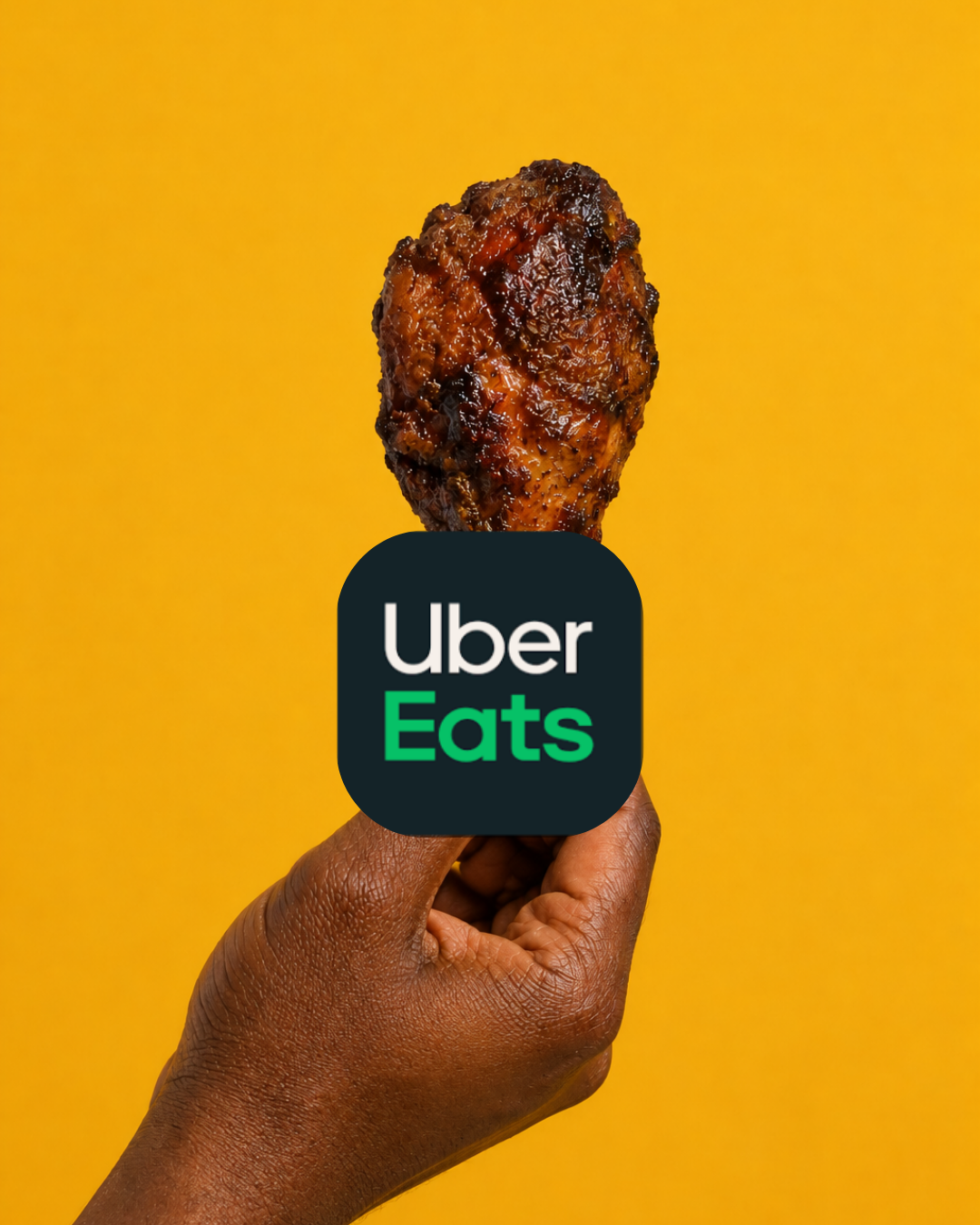 A hand holding a fried chicken drumstick with the Uber Eats logo on it, against a yellow background.