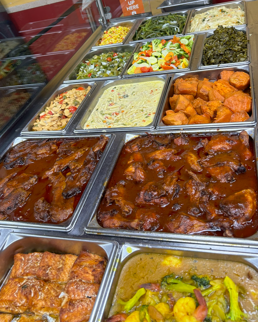 Assorted hot and cold dishes at a buffet, including cooked chicken in sauce, vegetables, salads, and stews.