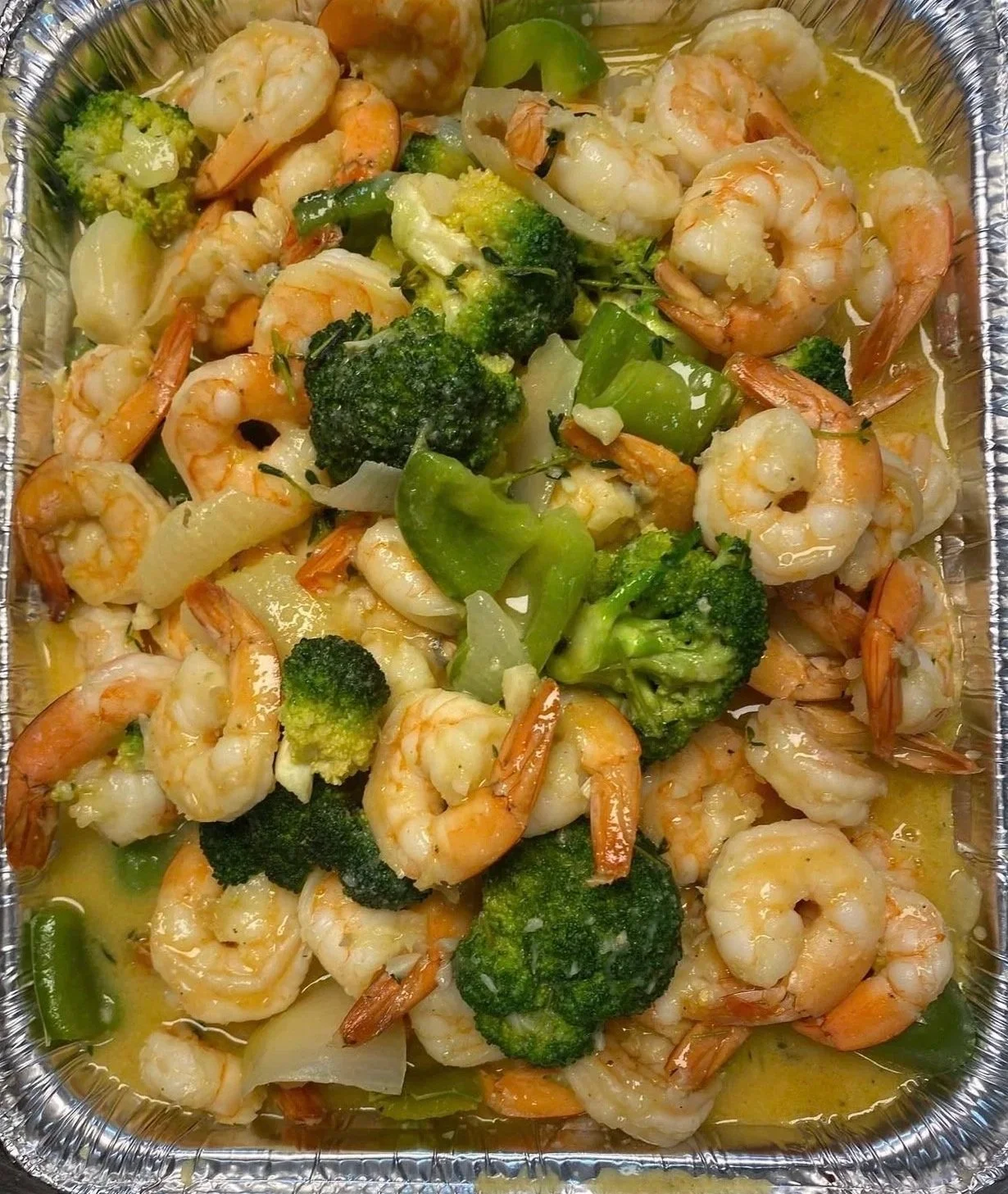 Cooked shrimp with broccoli, onions, and green peppers in a container.