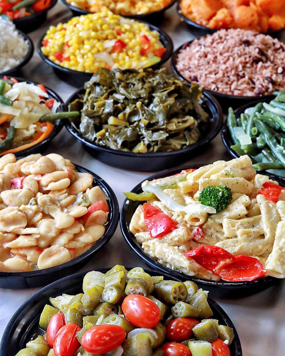 Assorted bowls of Southern-style side dishes including collard greens, macaroni salad, green beans, roasted tomatoes, potato salad, rice, and corn salad.